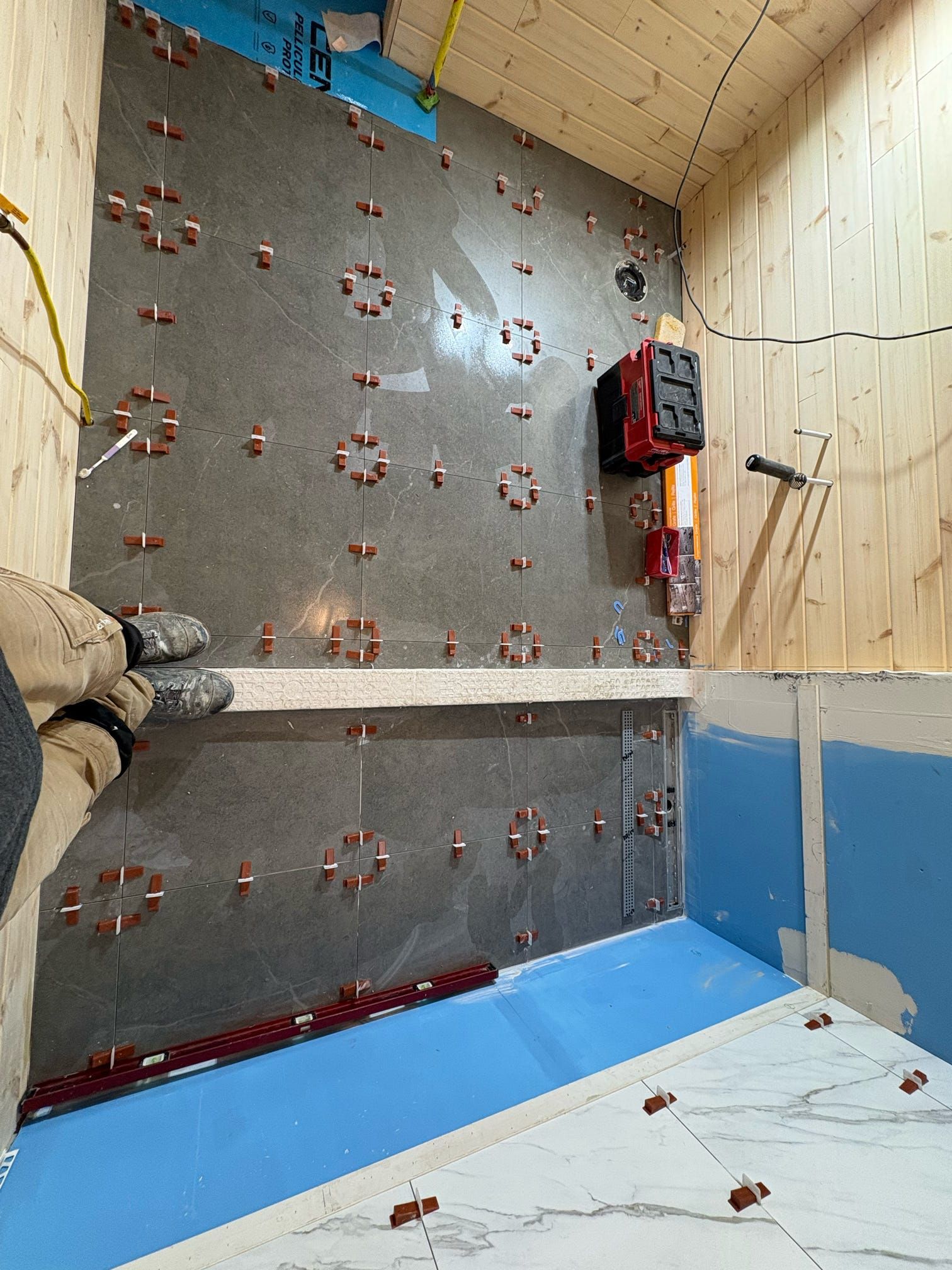Mur d'escalade intérieur avec panneaux gris, prises rouges et sol rembourré bleu sous un plafond beige