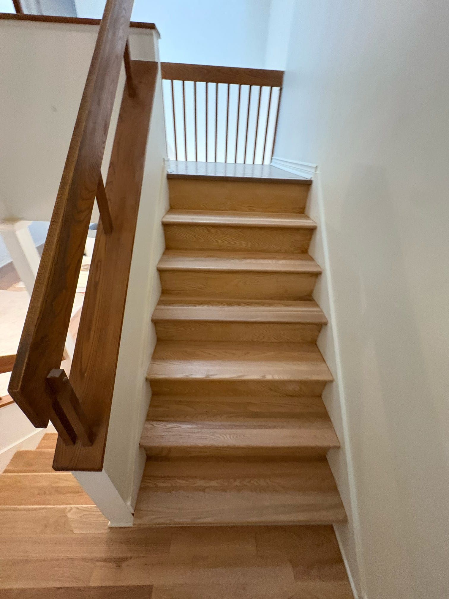 Un escalier en bois avec une rampe mène à un palier lumineux.