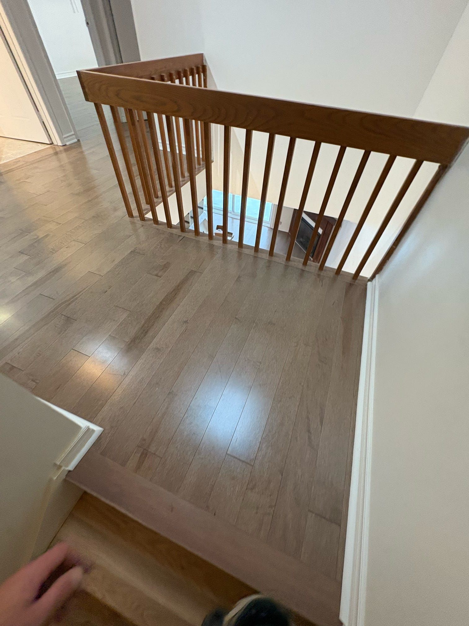 Palier d'escalier avec parquet clair et rampe marron donnant sur un niveau inférieur