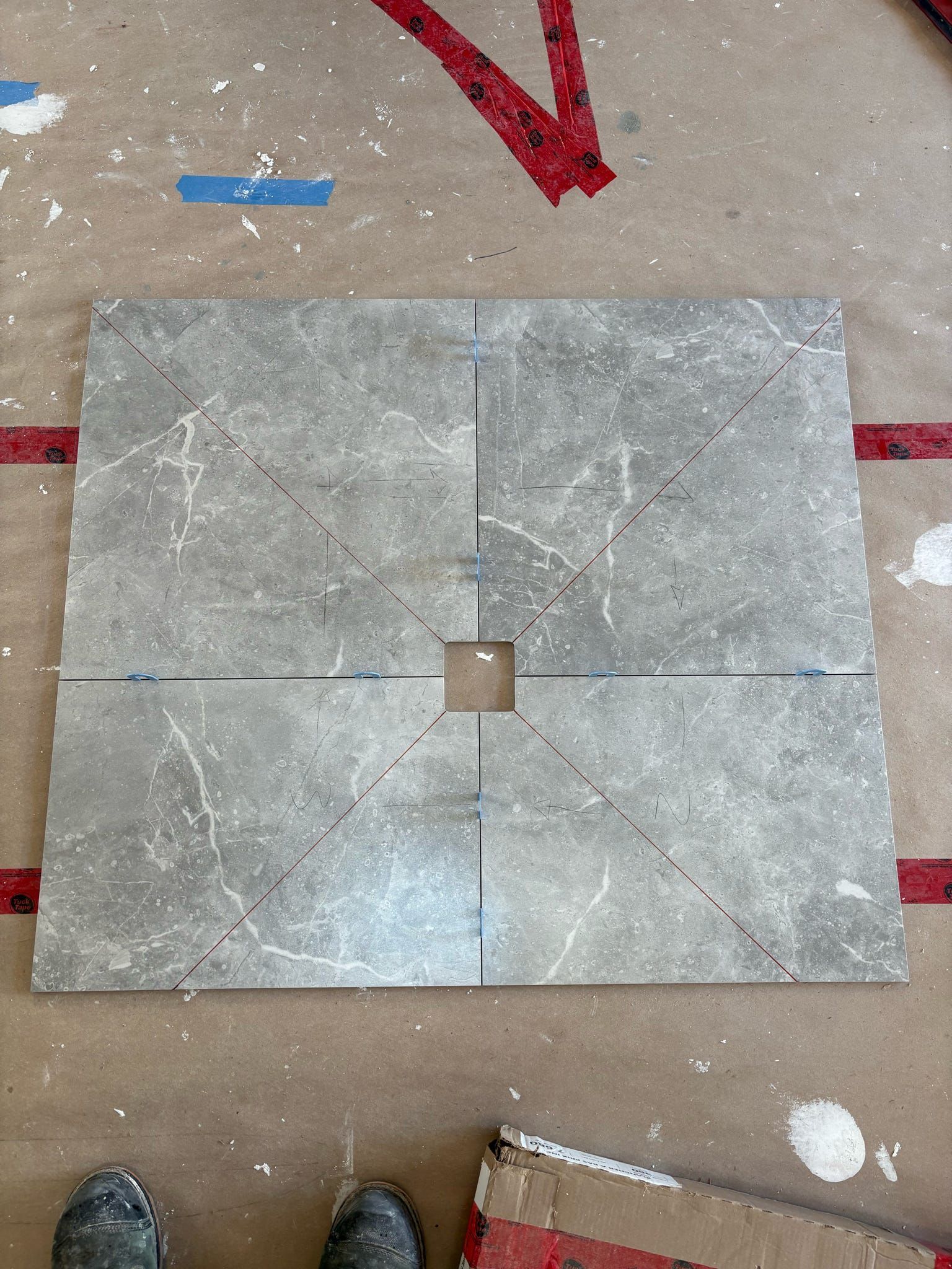 Carrelage de sol carré gris avec une petite découpe carrée au centre et marquée par des flèches rouges sur une surface de travail