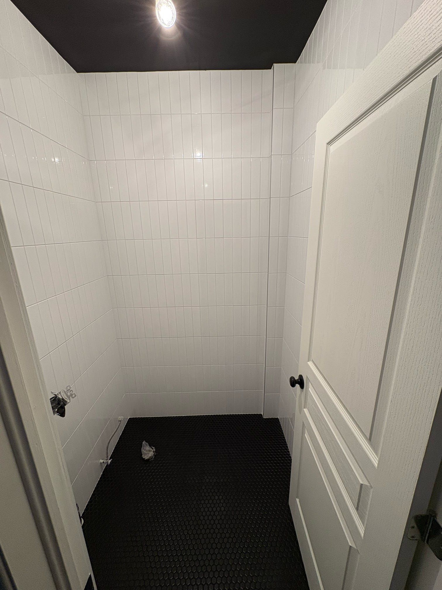 Petite cabine de toilettes carrelée de blanc avec sol foncé, vue à travers une porte ouverte.