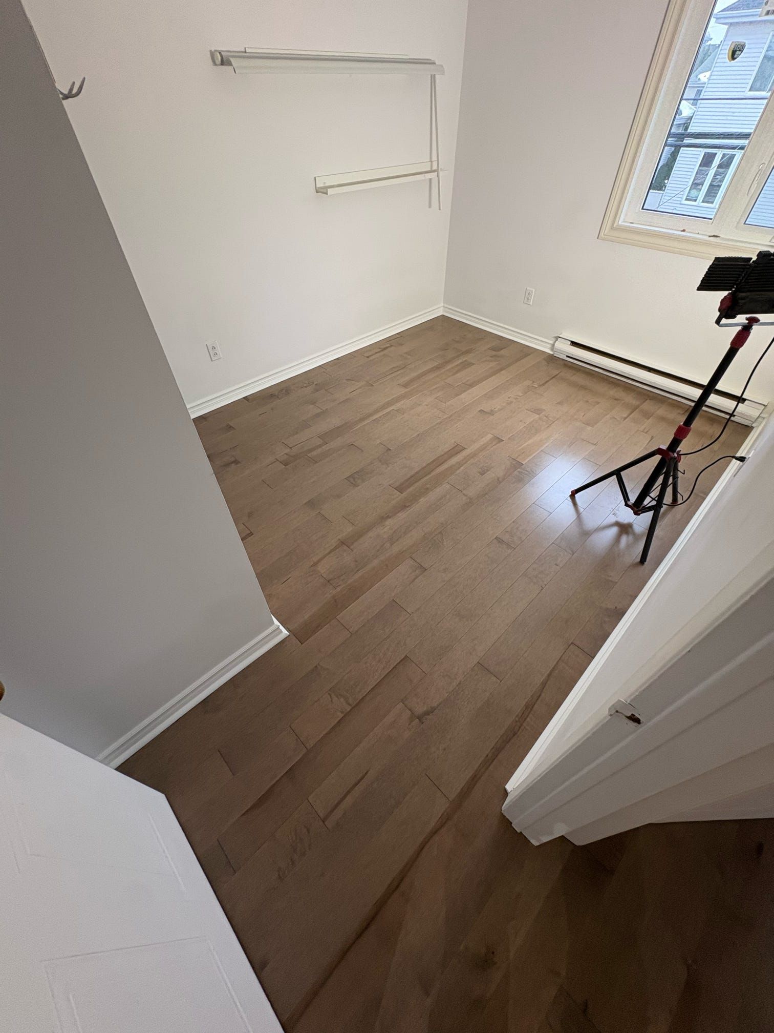 Petite pièce blanche vide avec parquet, étagères murales et une fenêtre laissant entrer la lumière du jour.