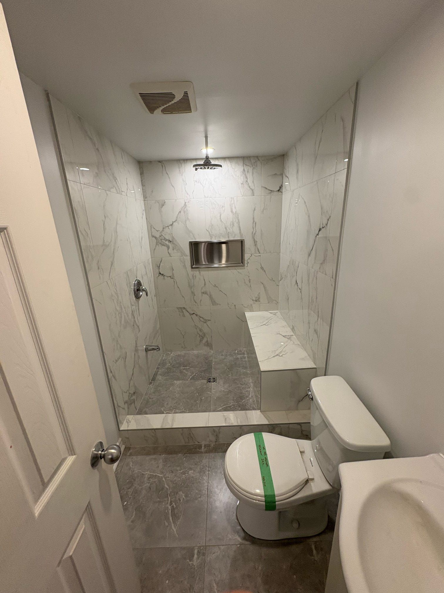 Petite salle de bains carrelée avec toilettes, cabine de douche et meuble-lavabo blanc.