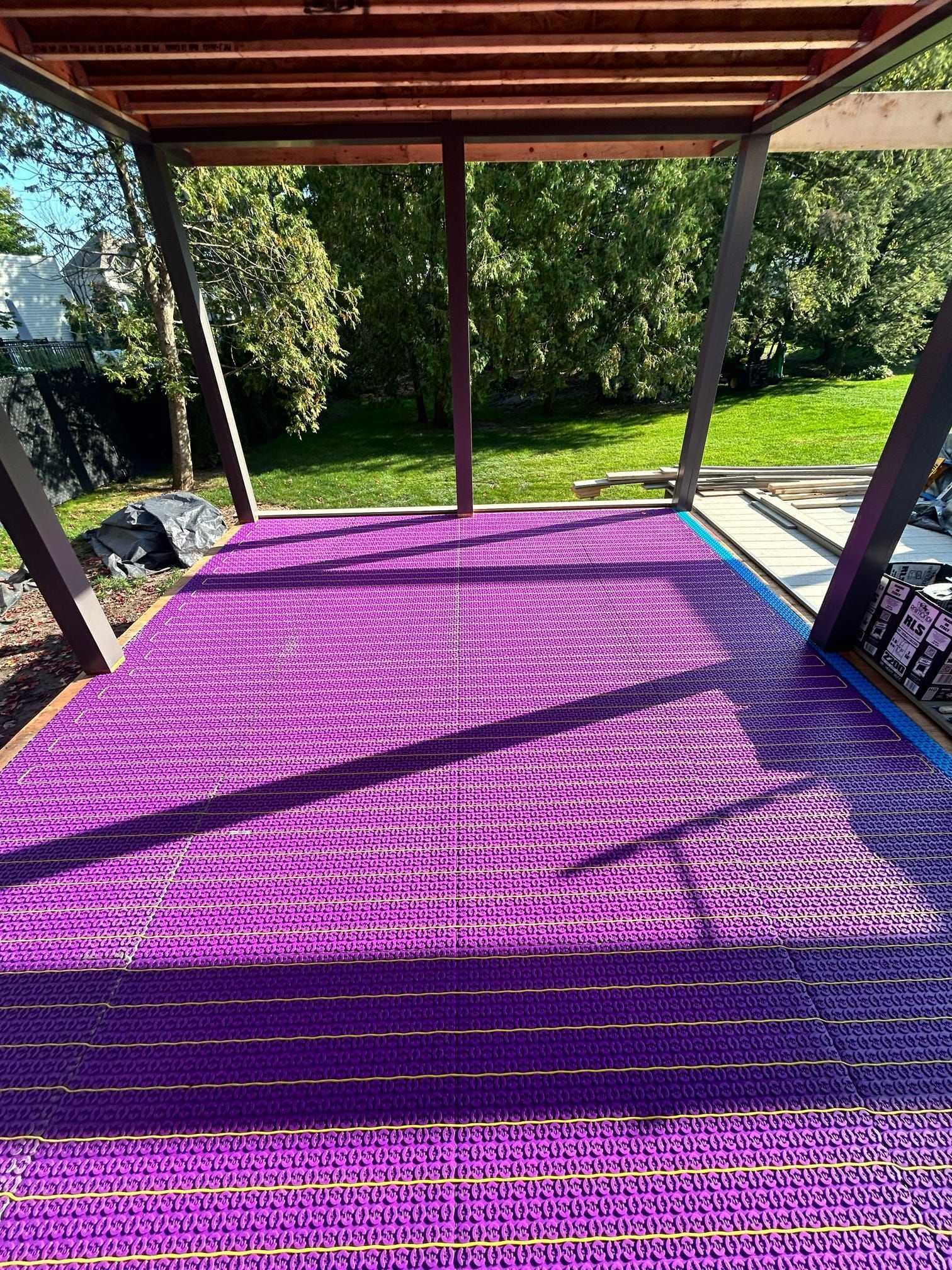 Tapis violet sur une terrasse en bois ombragée donnant sur une cour verdoyante et ensoleillée