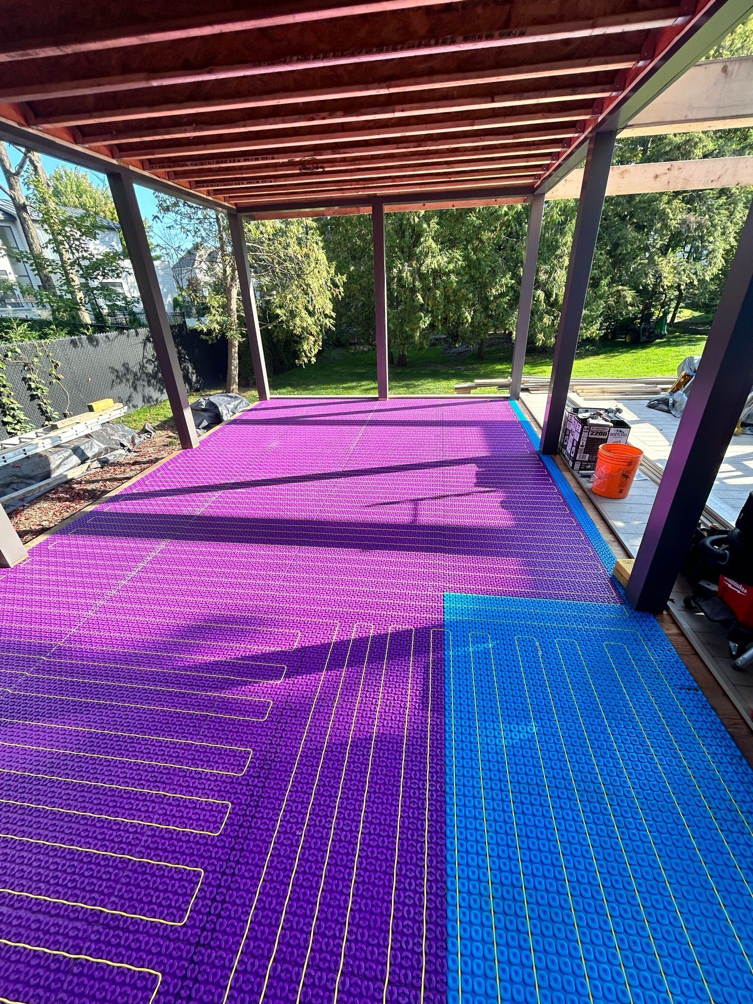 Terrasse couverte avec tapis de sol violets et bleus sous une pergola en bois, à côté d'un jardin et de chaises longues
