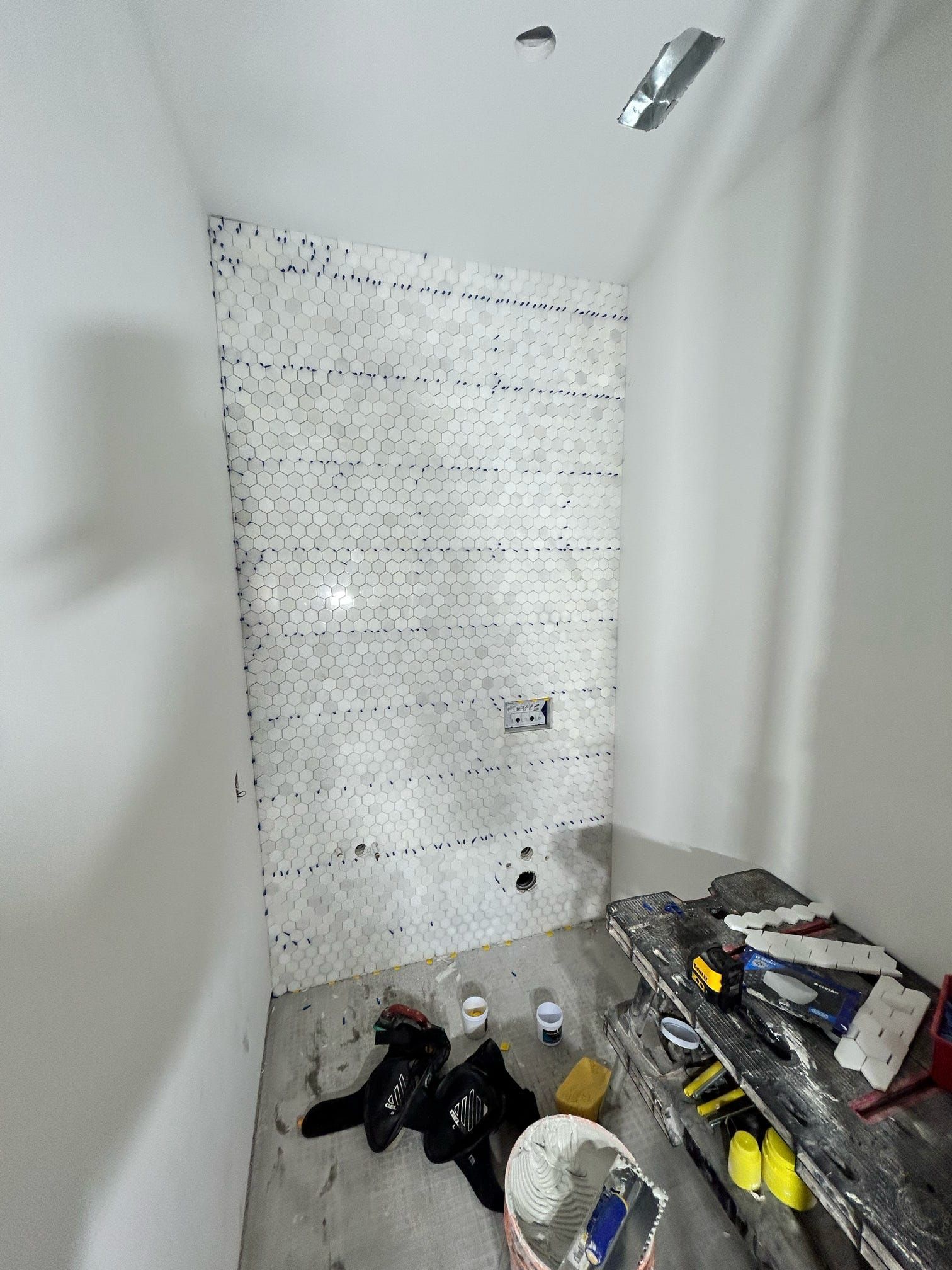 Petite cabine de douche carrelée avec outils et fournitures éparpillés sur le sol pendant les travaux de rénovation.