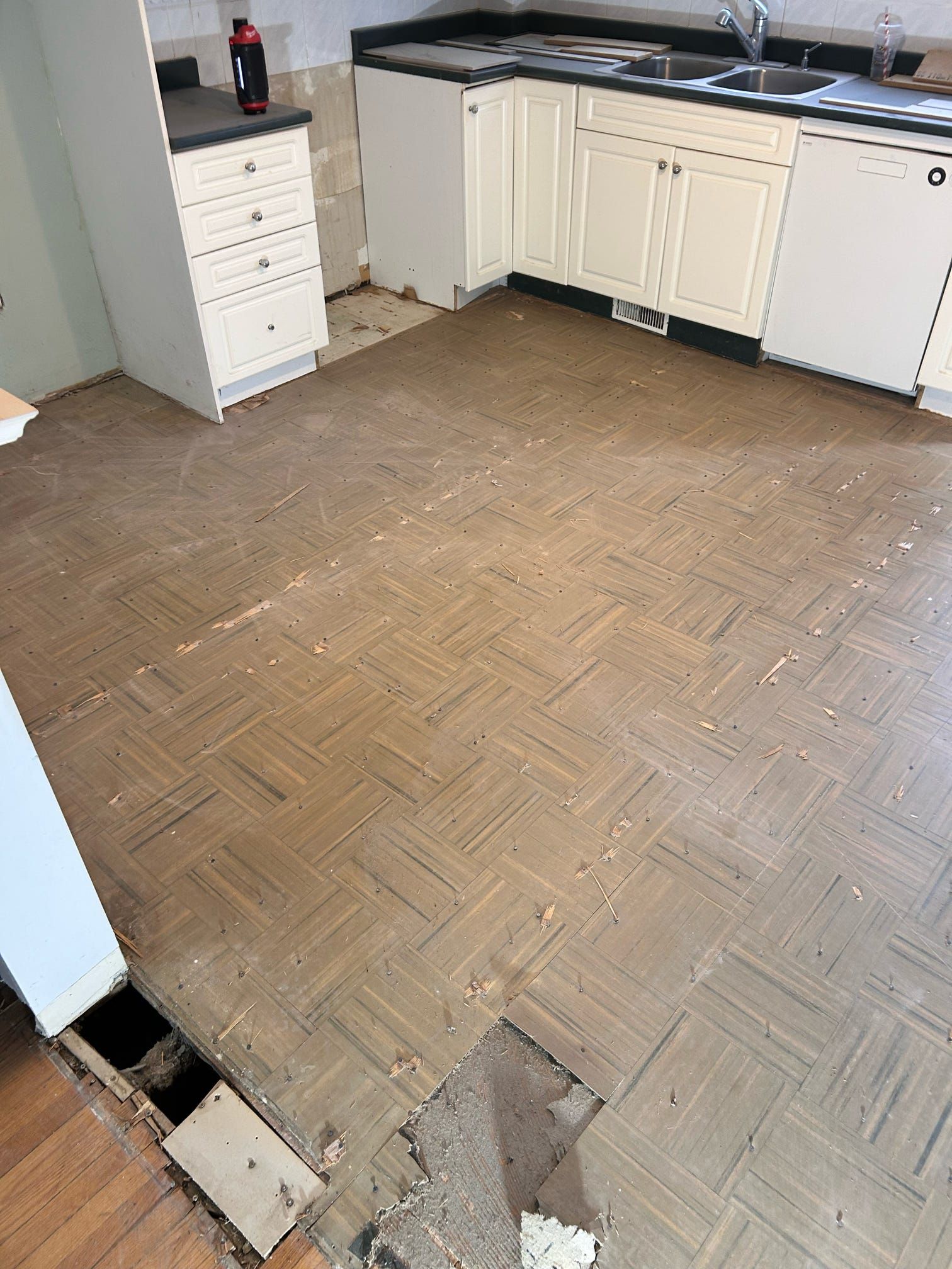 Sol de cuisine endommagé, parquet manquant et placards le long du mur