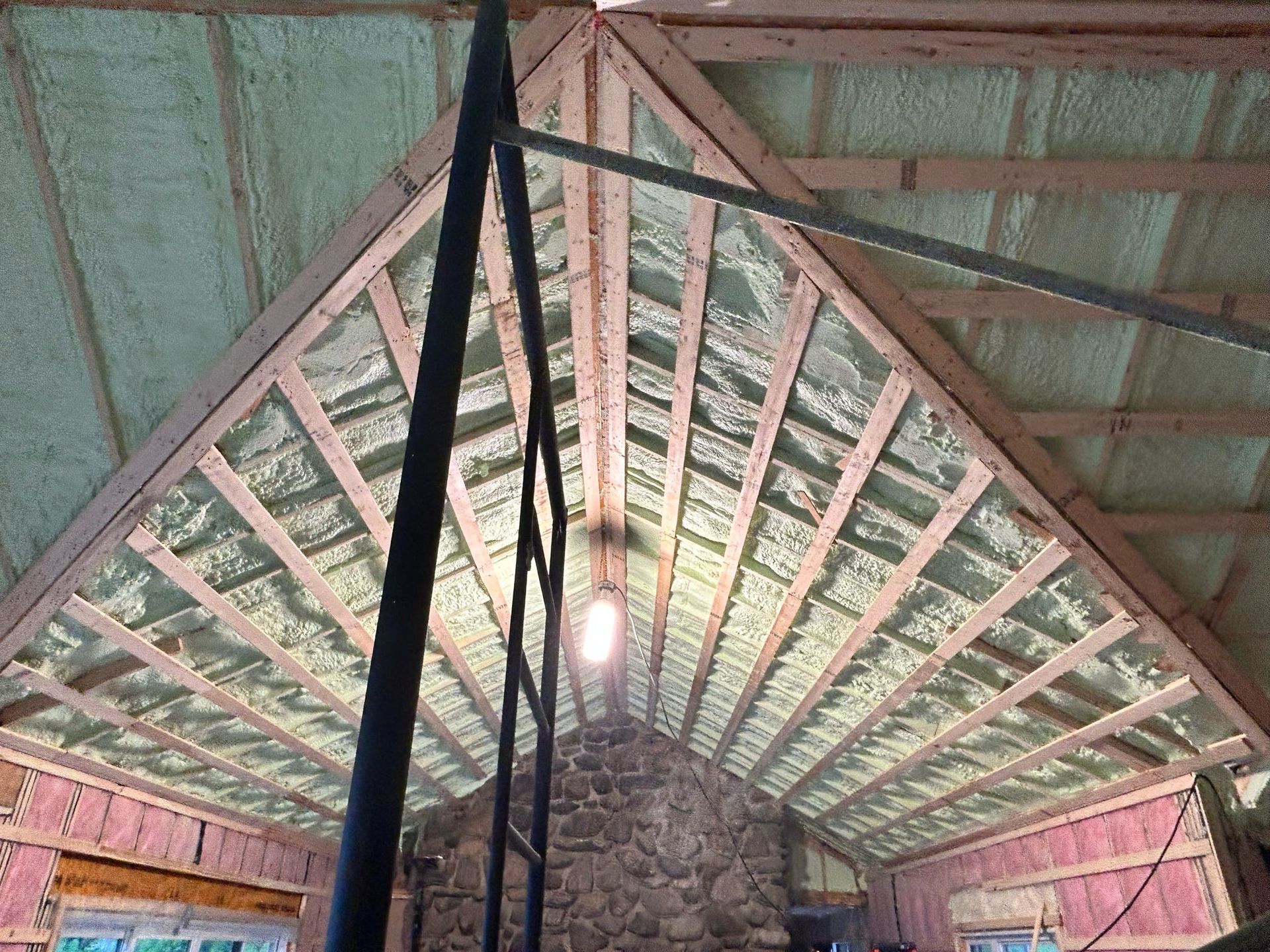 Intérieur d'une cabane rustique en forme de A avec poutres apparentes, mur en pierre et ampoule suspendue.