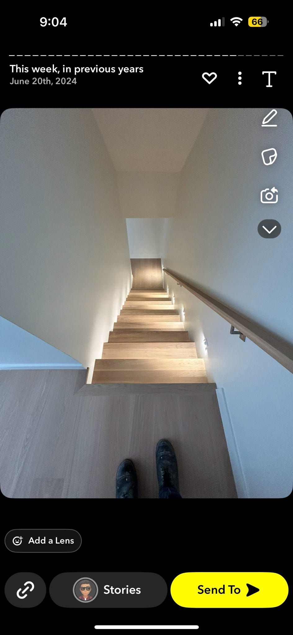 Vue plongeante sur un escalier étroit aux marches en bois, aux murs blancs et à la rampe ; des chaussures sont visibles en bas.