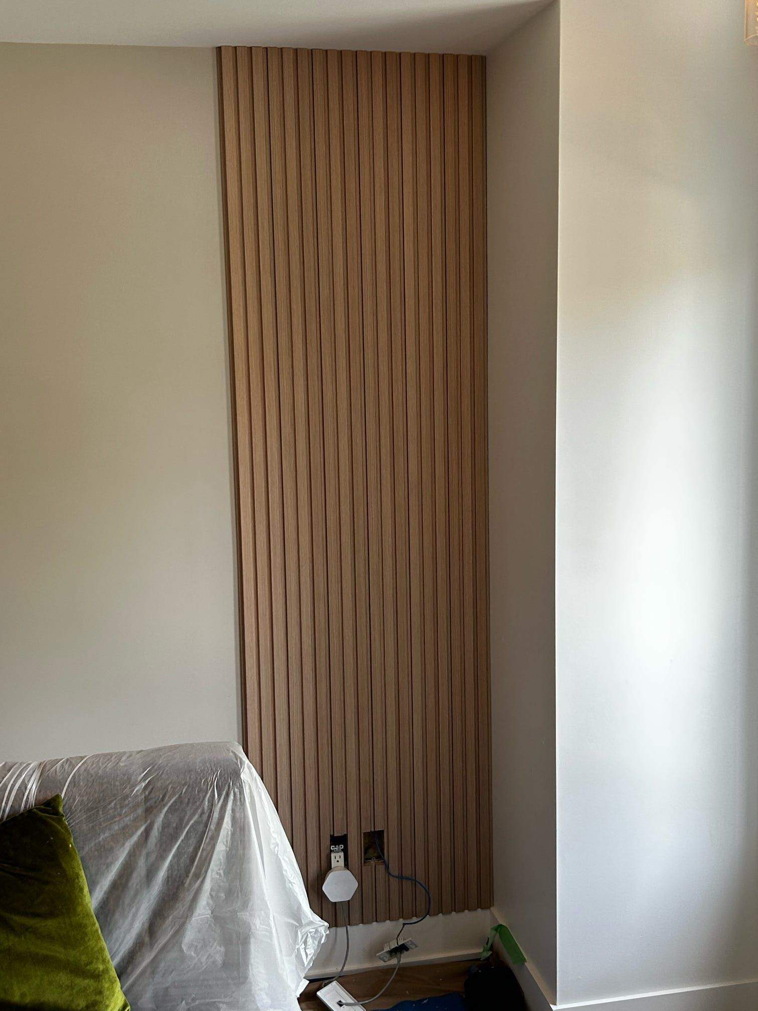 Un petit coin de pièce avec un panneau en lattes de bois du sol au plafond, des murs blancs et une chaise recouverte au premier plan