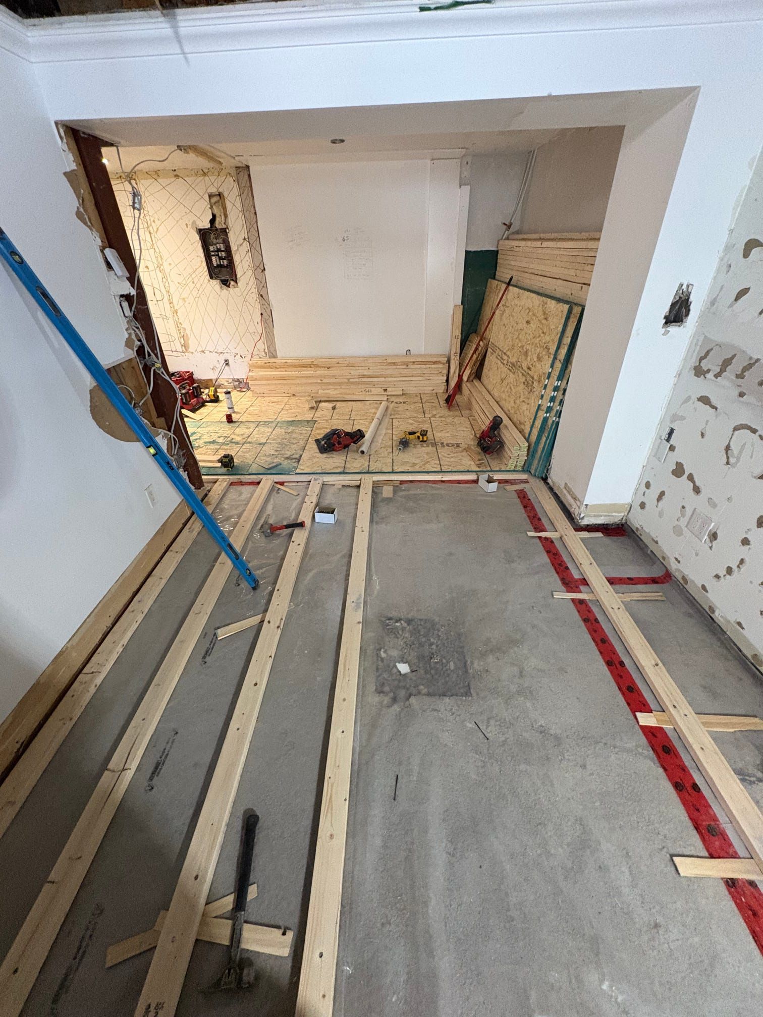 Chantier de rénovation avec solives apparentes, débris et une porte donnant sur une pièce inachevée