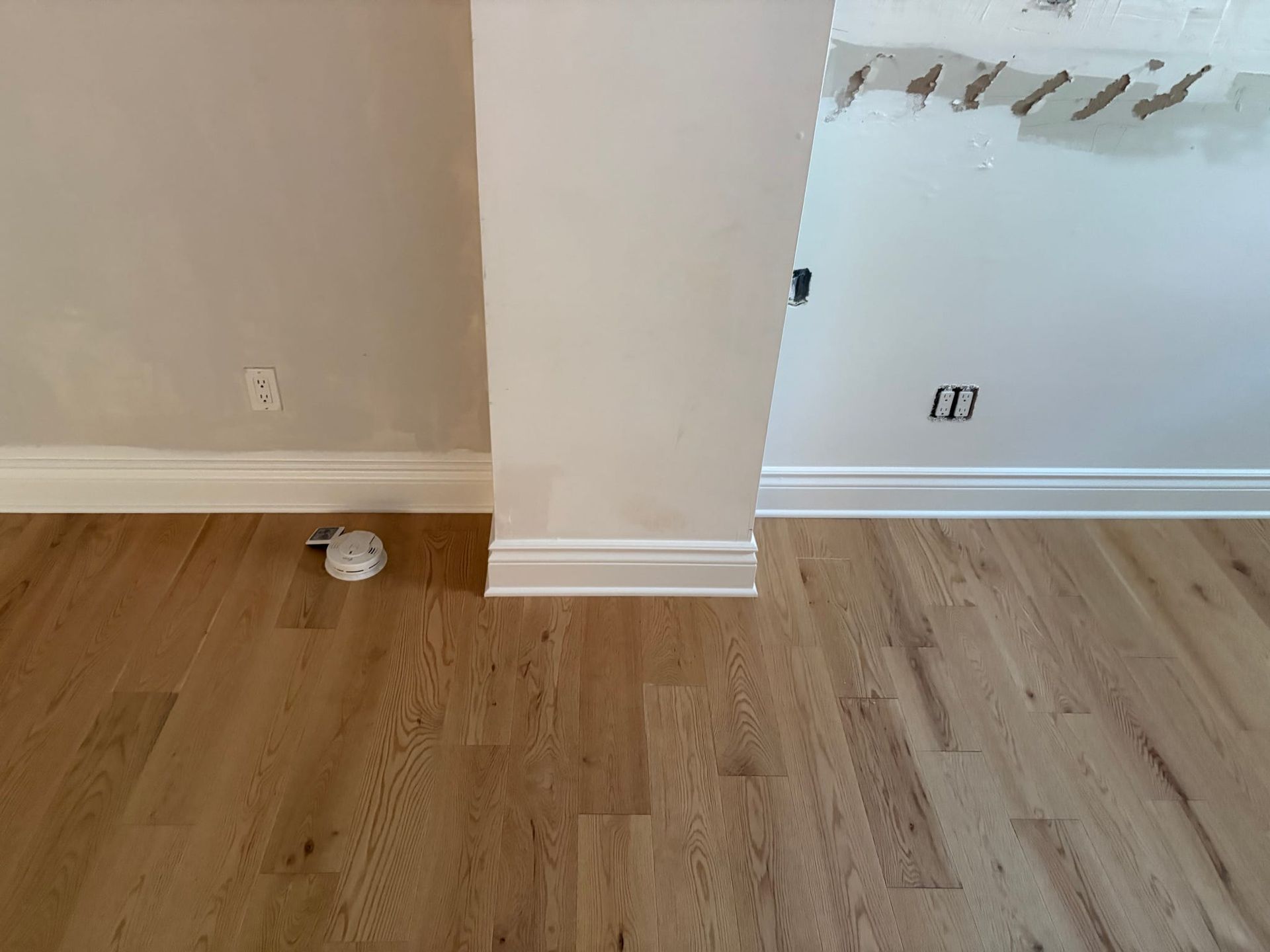 Pièce vide avec parquet clair, murs beiges et une colonne centrale près d'une ouverture