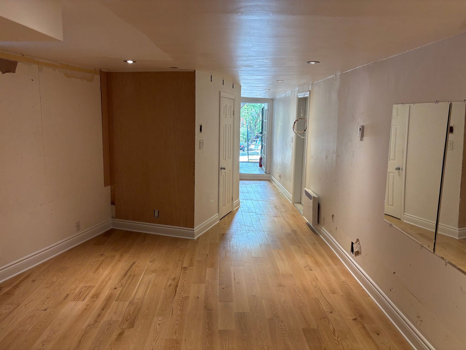 Pièce étroite et vide, avec parquet, murs beiges et lumière provenant d'une fenêtre au fond.