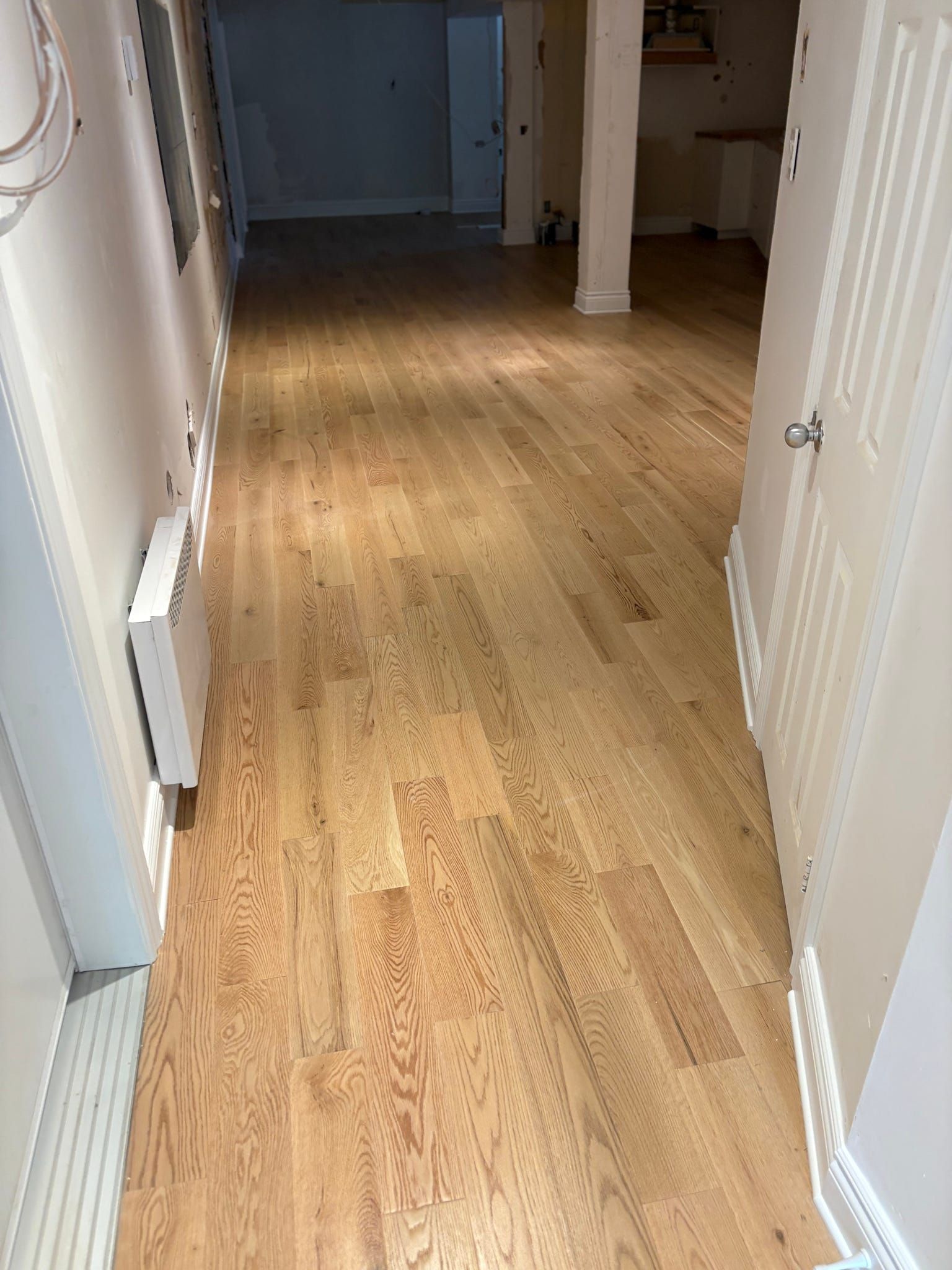 Couloir étroit avec parquet clair, murs blancs et une porte au fond.