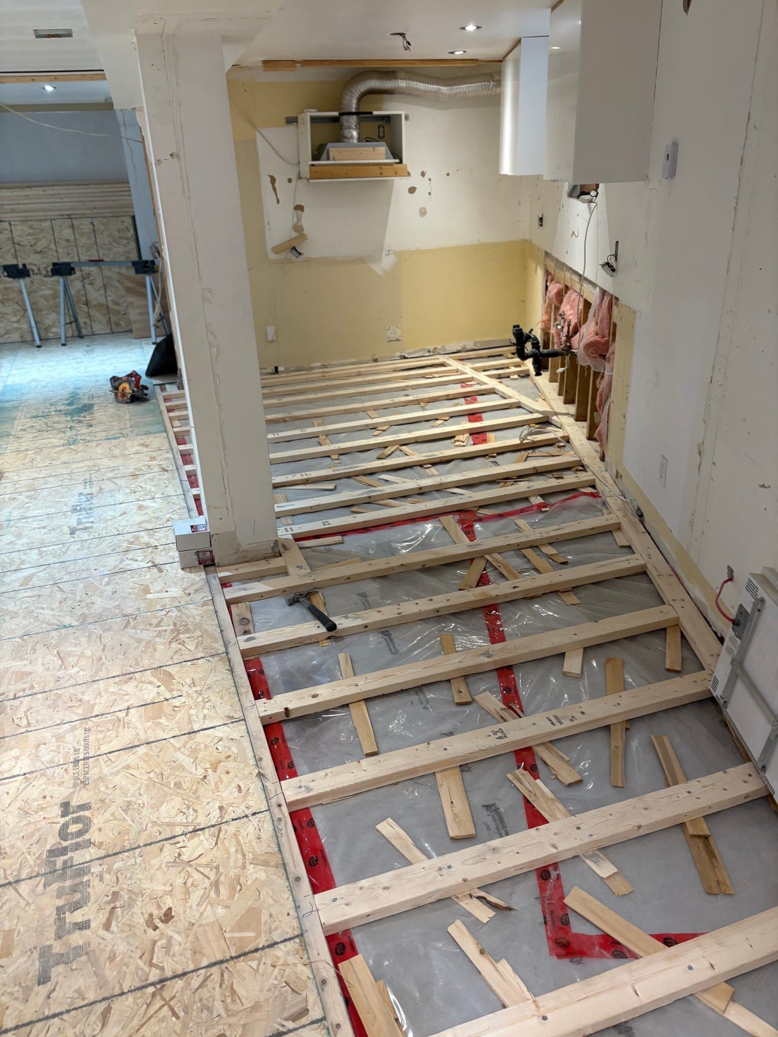 Le revêtement de sol de la cuisine a été retiré lors des travaux de rénovation, laissant apparaître les solives et la structure du sous-plancher.