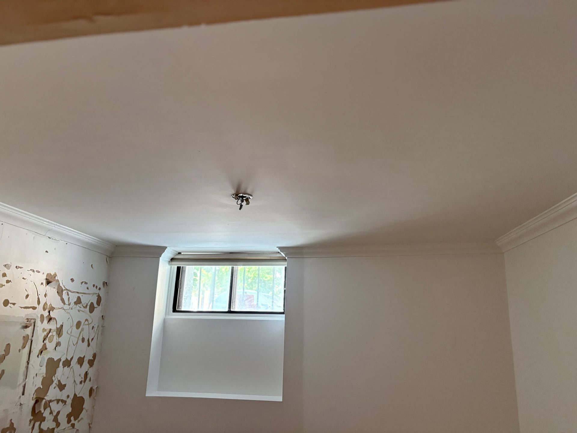 Petite pièce aux murs blancs, au plafond bas et dotée d'une petite fenêtre au-dessus d'un cache-radiateur.