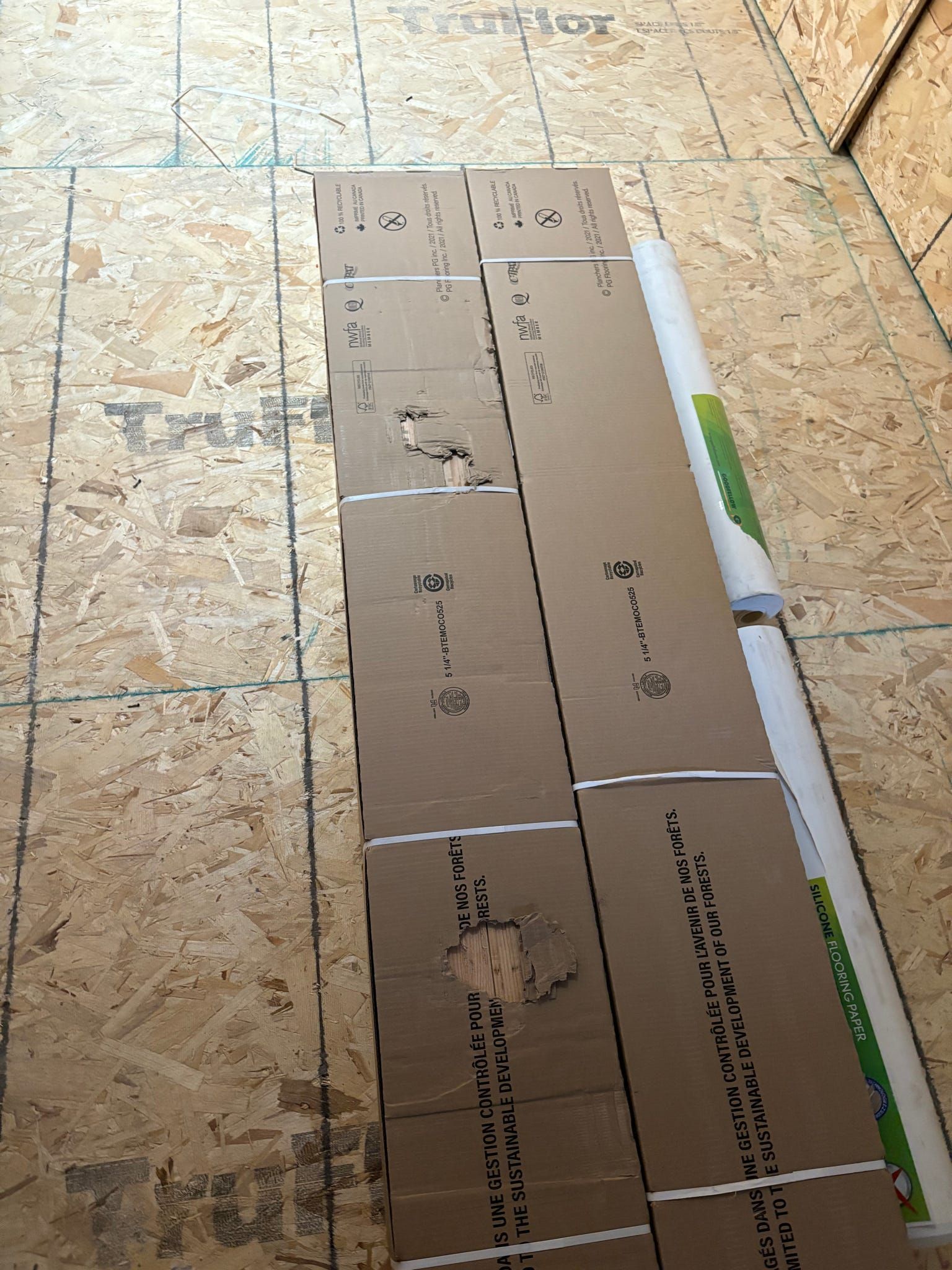 Gabarit en carton découpé, posé sur un sol carrelé à côté d'une affiche roulée ou d'un tube en carton.