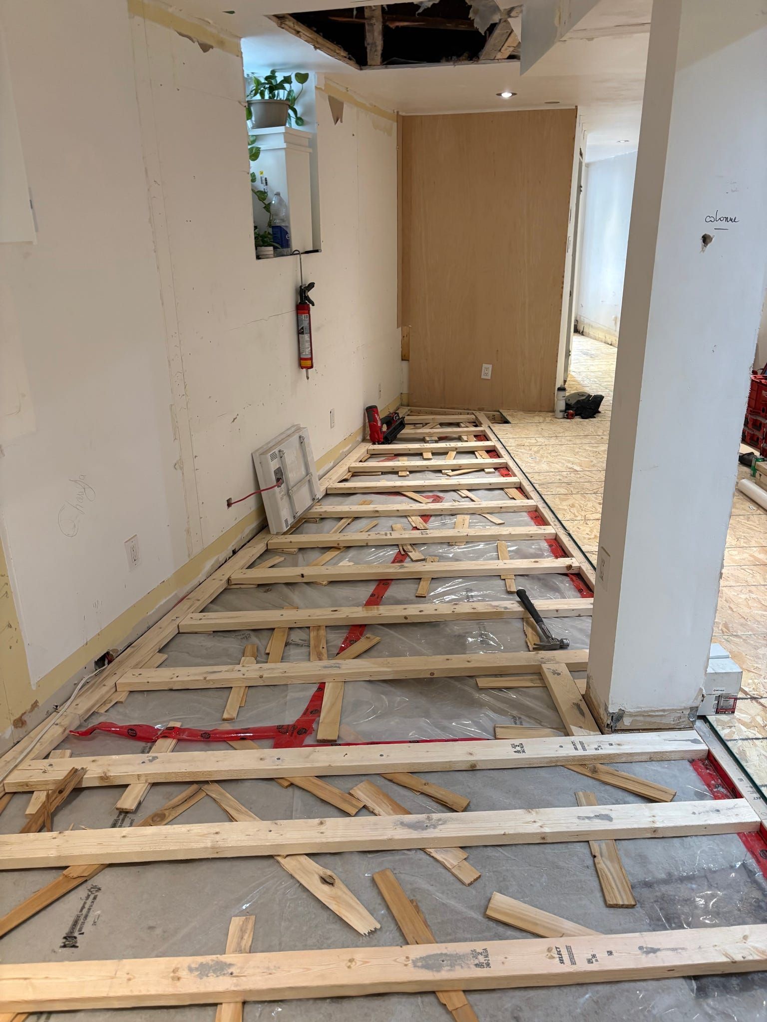 Couloir en rénovation avec solives apparentes, débris et une porte au fond.