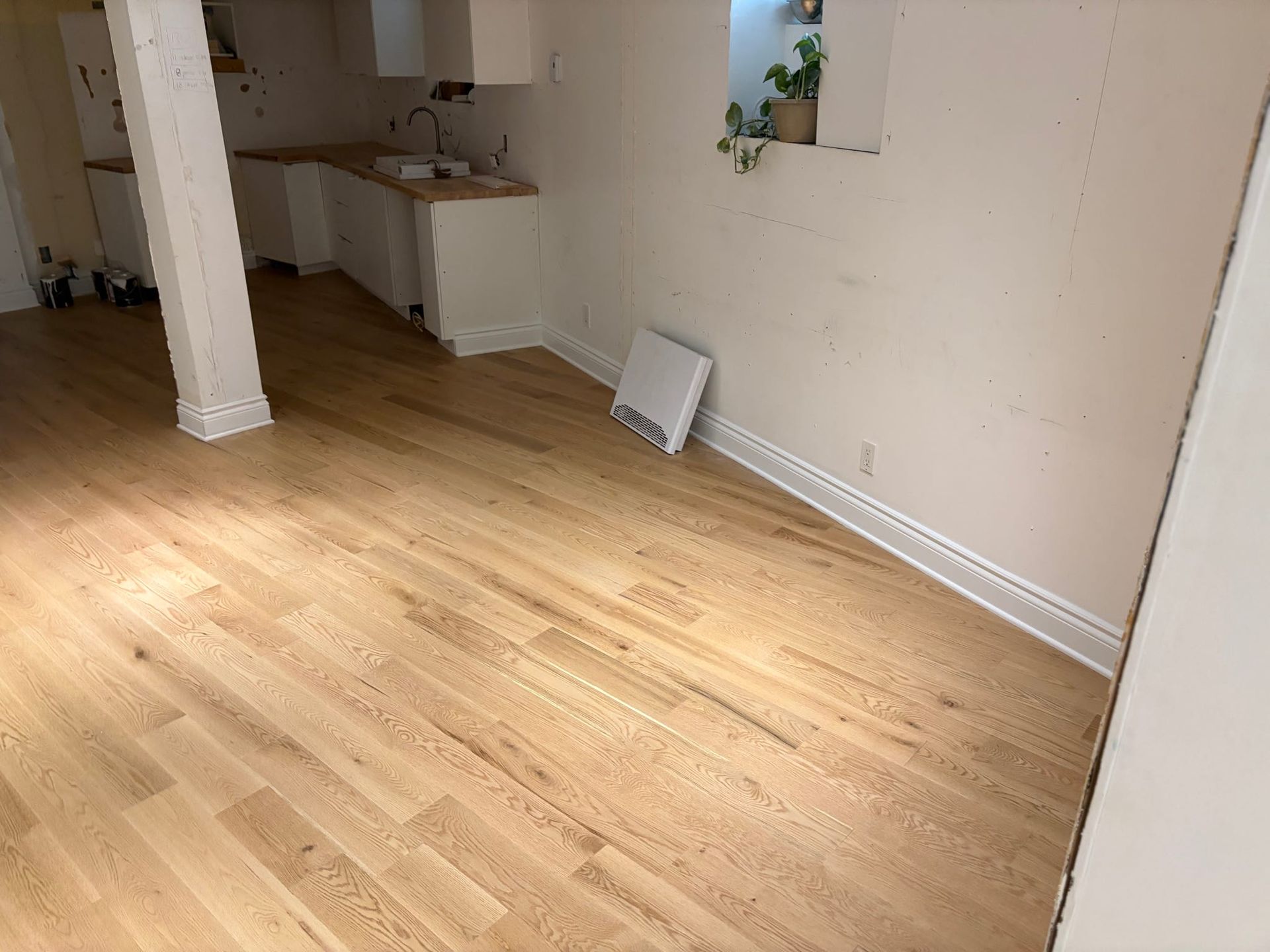Pièce vide avec parquet clair, murs blancs et un petit coin cuisine au fond.