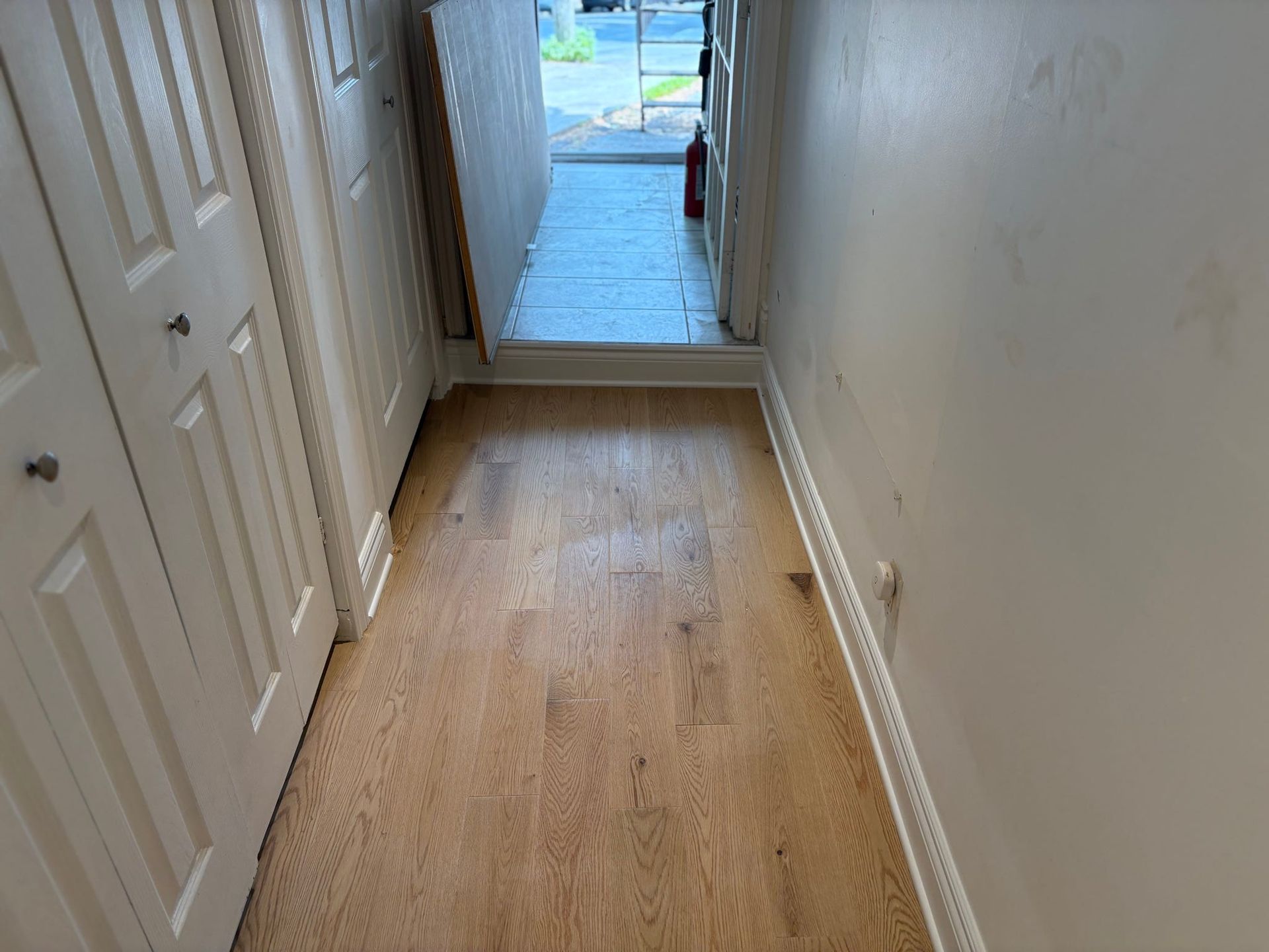Couloir étroit avec parquet, murs blancs et éclairage de la porte d'entrée au fond