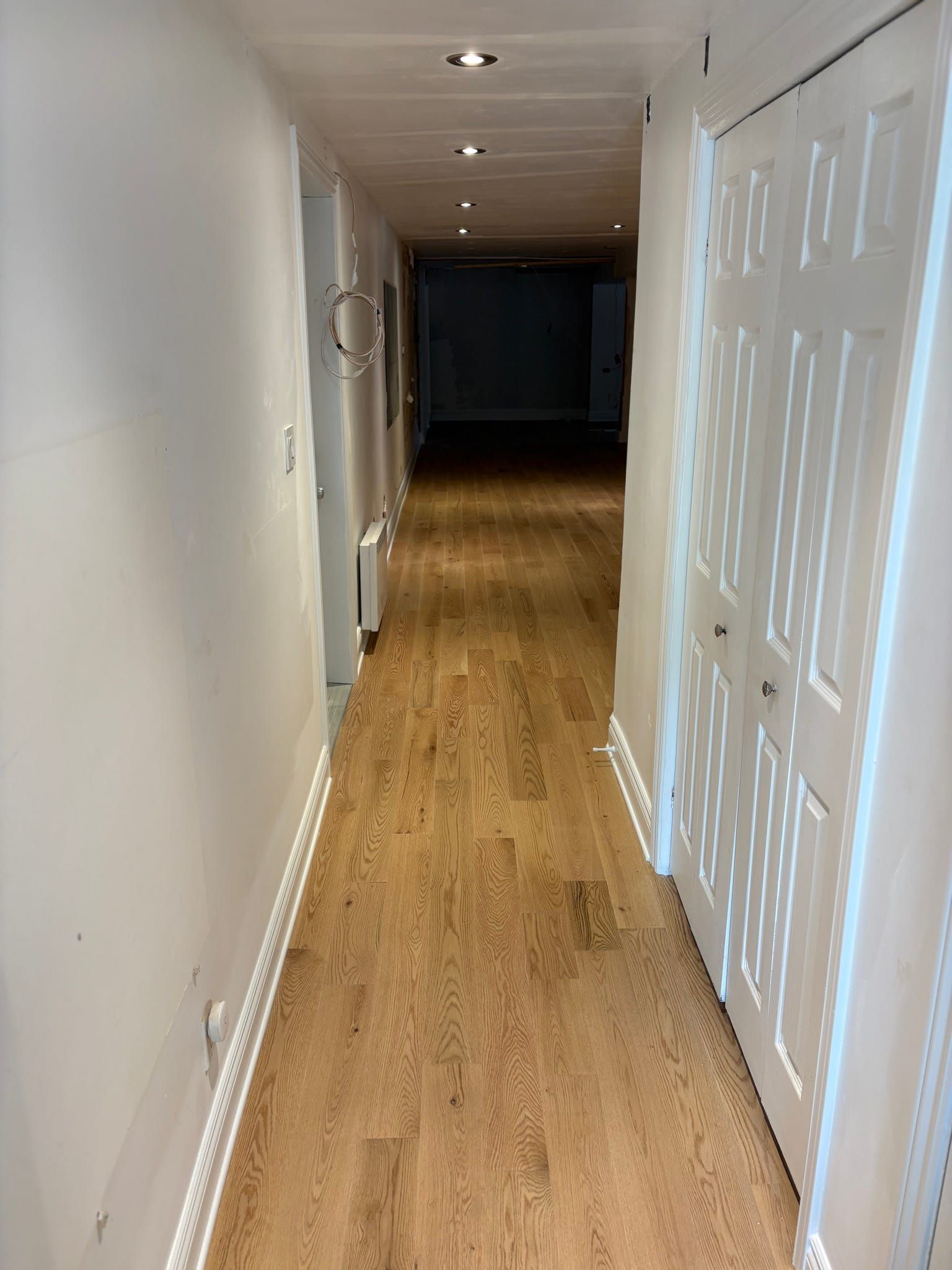 Couloir étroit avec parquet clair, murs blancs, spots encastrés au plafond et portes fermées sur la droite.
