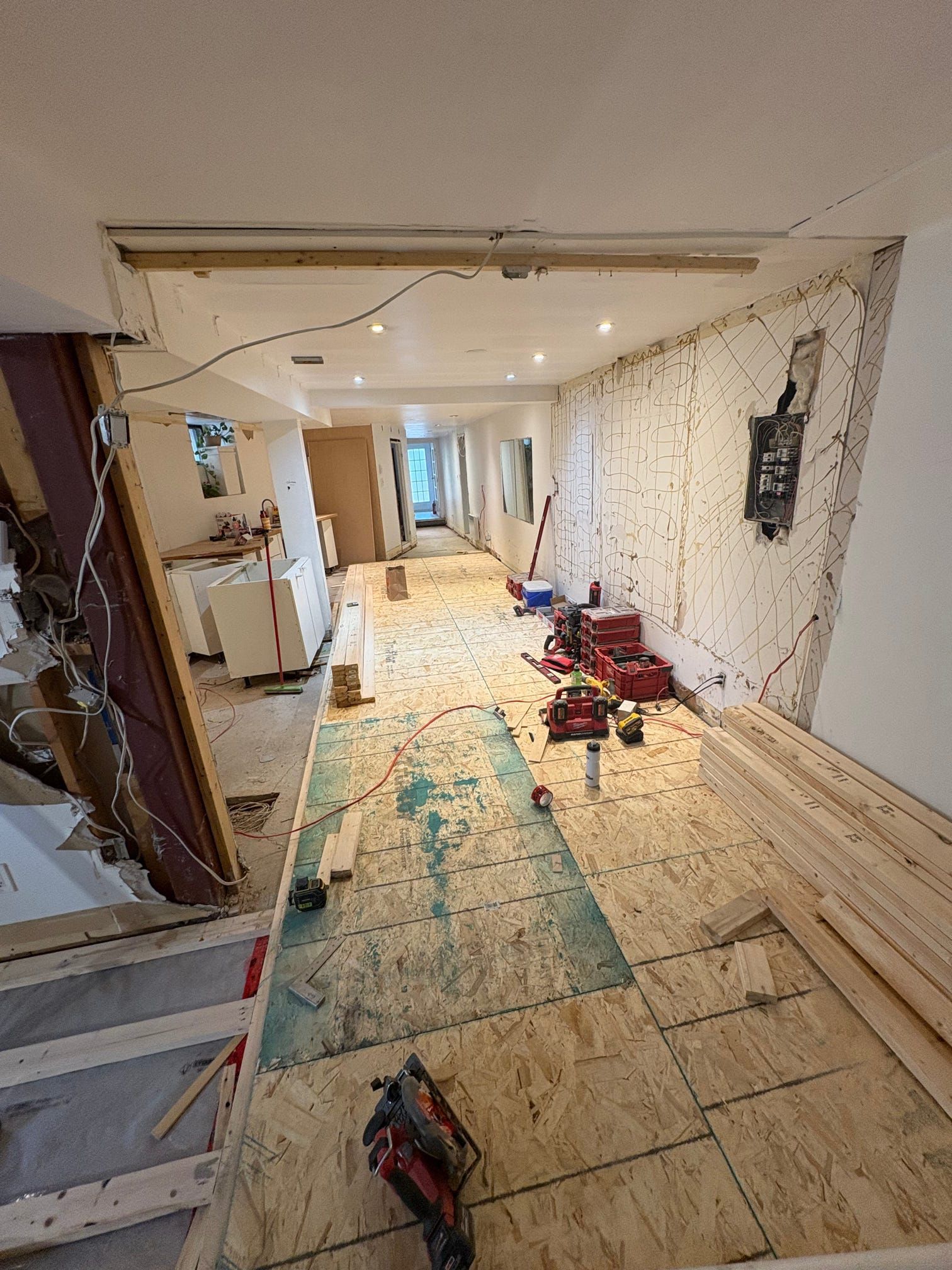 Travaux de rénovation en cours dans un couloir étroit avec un sol en contreplaqué apparent, des outils et des débris de construction.