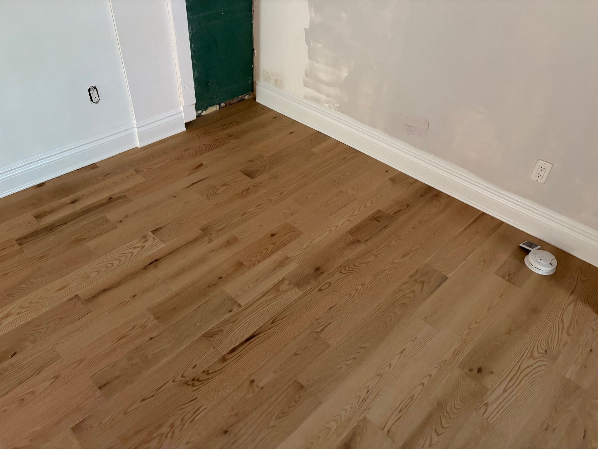 Pièce vide avec parquet clair, murs blancs et porte verte.