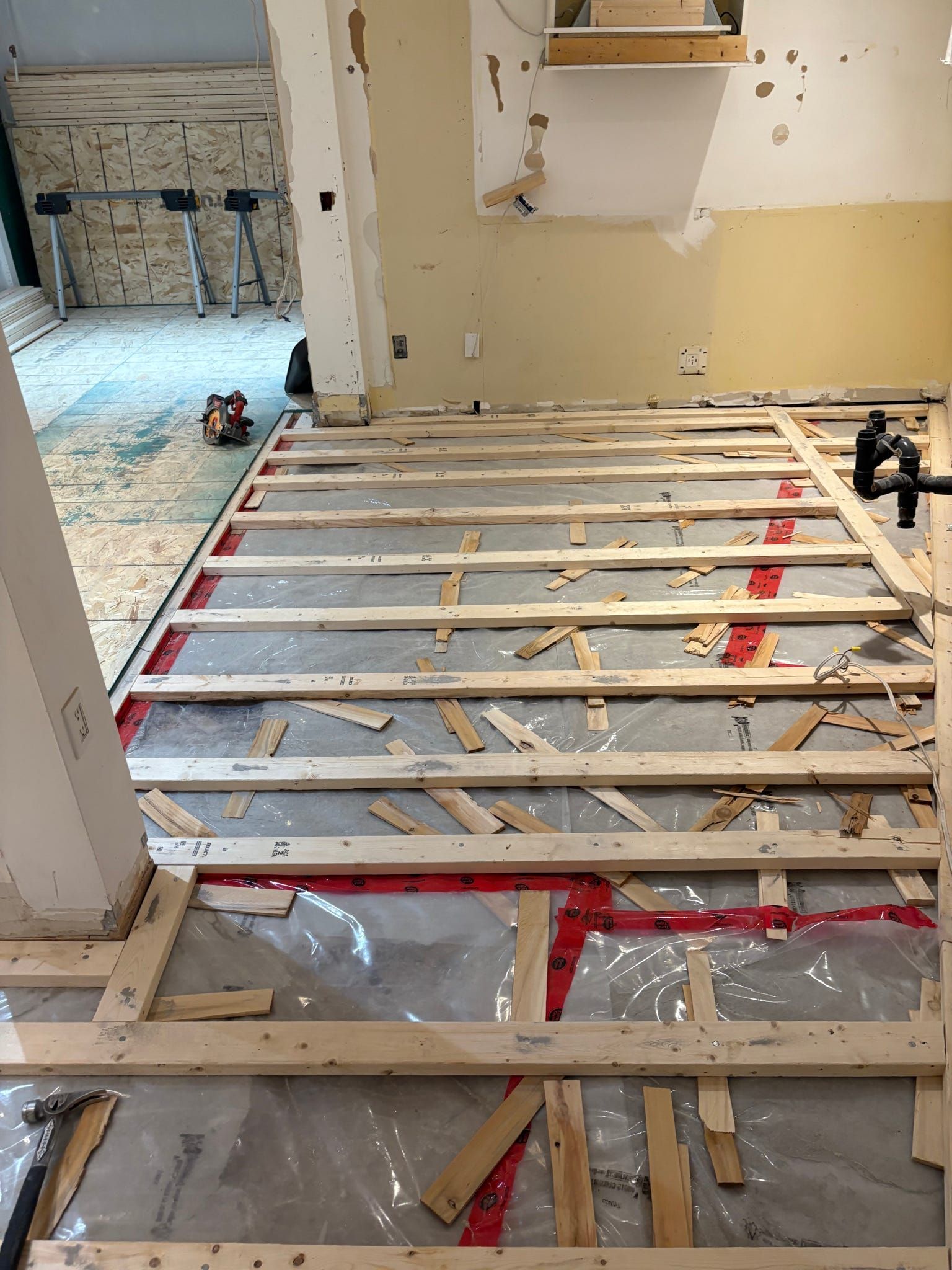 Solives apparentes et débris de construction dans une pièce partiellement rénovée avec une porte donnant sur une autre pièce.