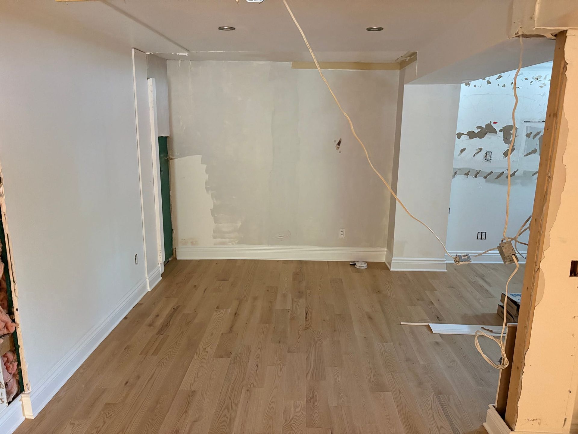 Pièce vide avec parquet, murs blancs et matériaux de construction apparents près d'une porte.