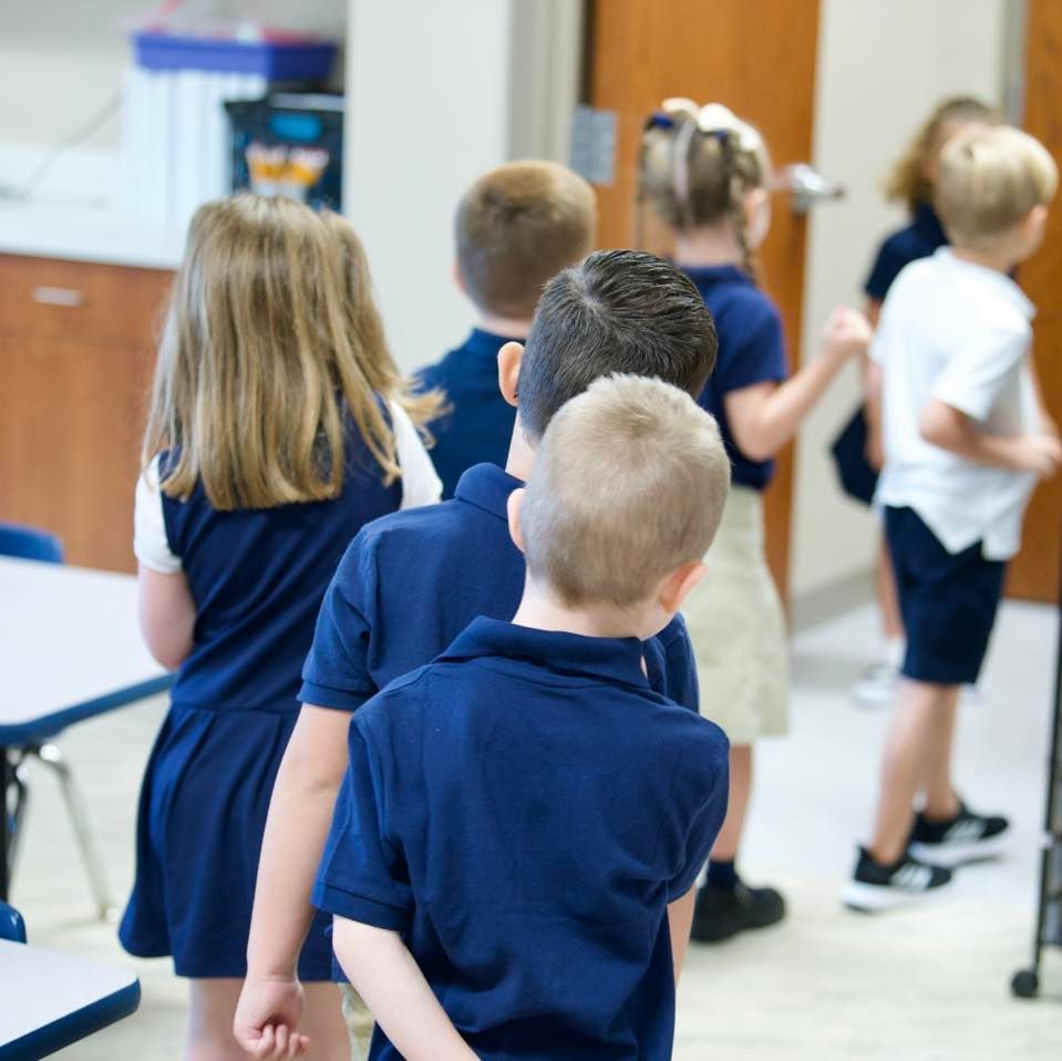 Children in blue uniforms standing in a line in a classroom.