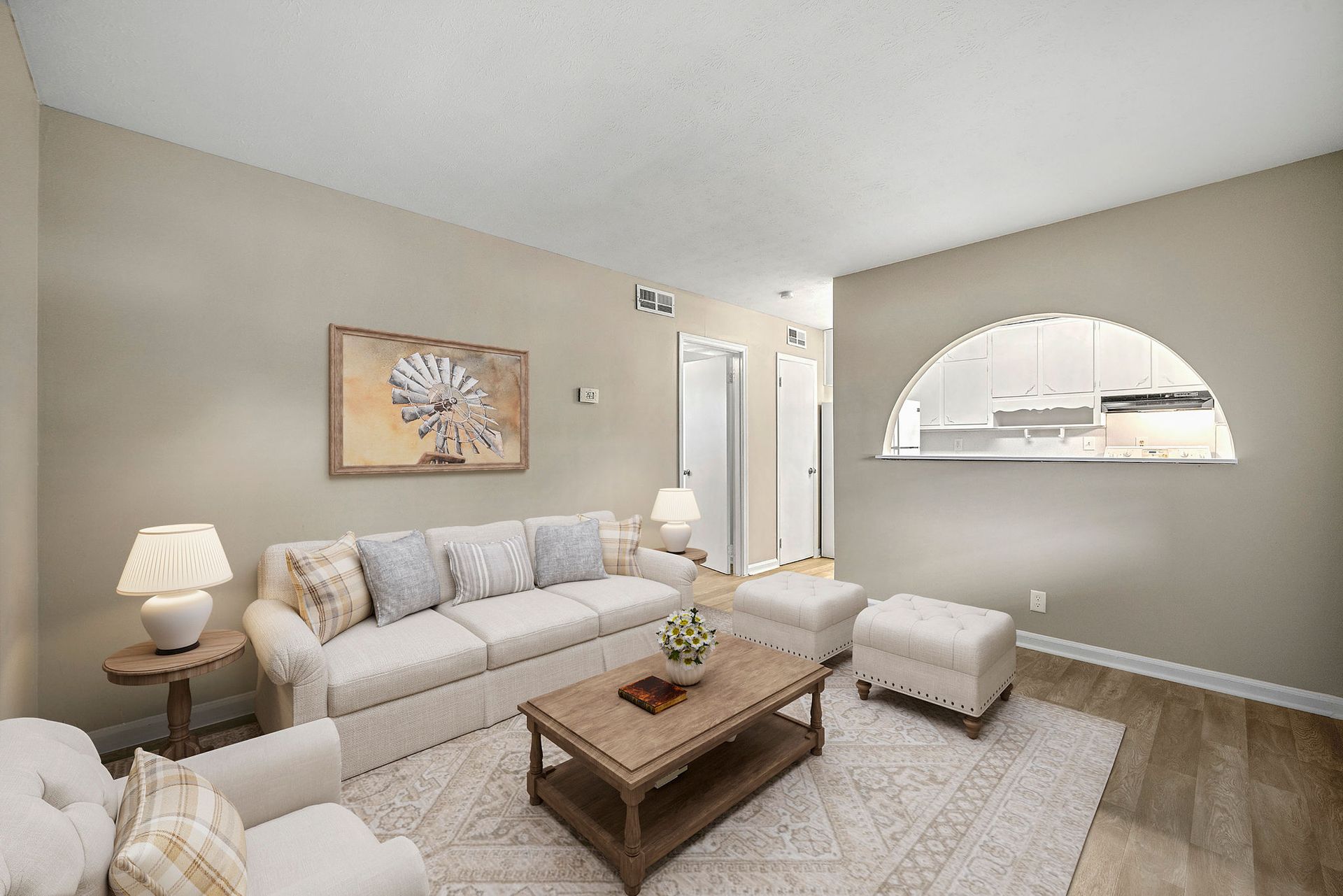 Bright living room with beige sofa, coffee table, armchair, lamp, and arched pass-through window.