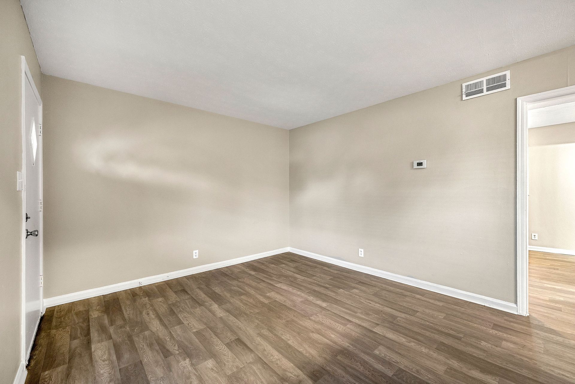 Empty beige room with wood flooring and a doorway on the right.