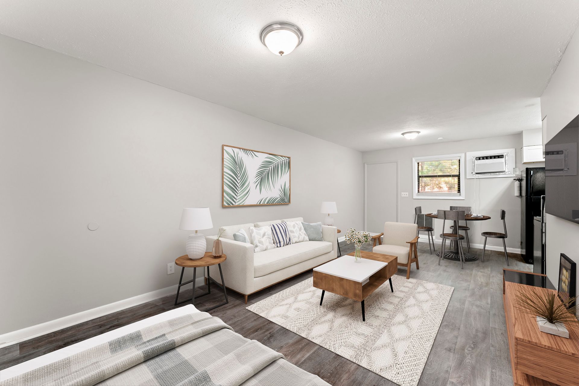 Bright living room with white sofa, coffee table, rug, and desk area near a window.