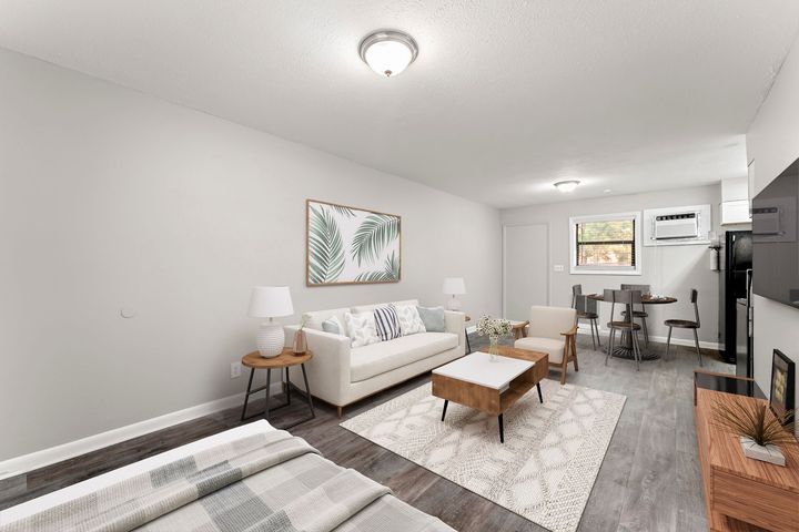 Bright living room with white sofa, coffee table, rug, and desk area near a window.