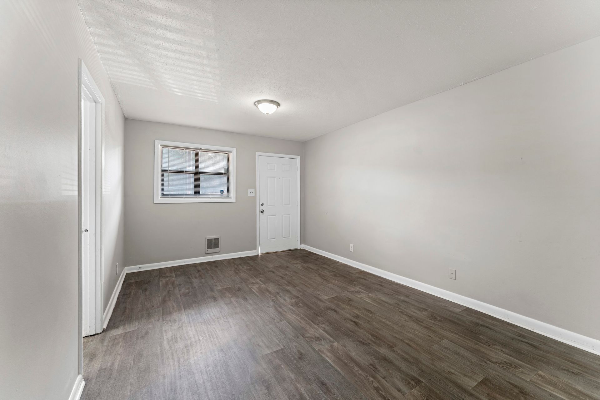 Empty white room with gray wood floors, a window, and a closed door.