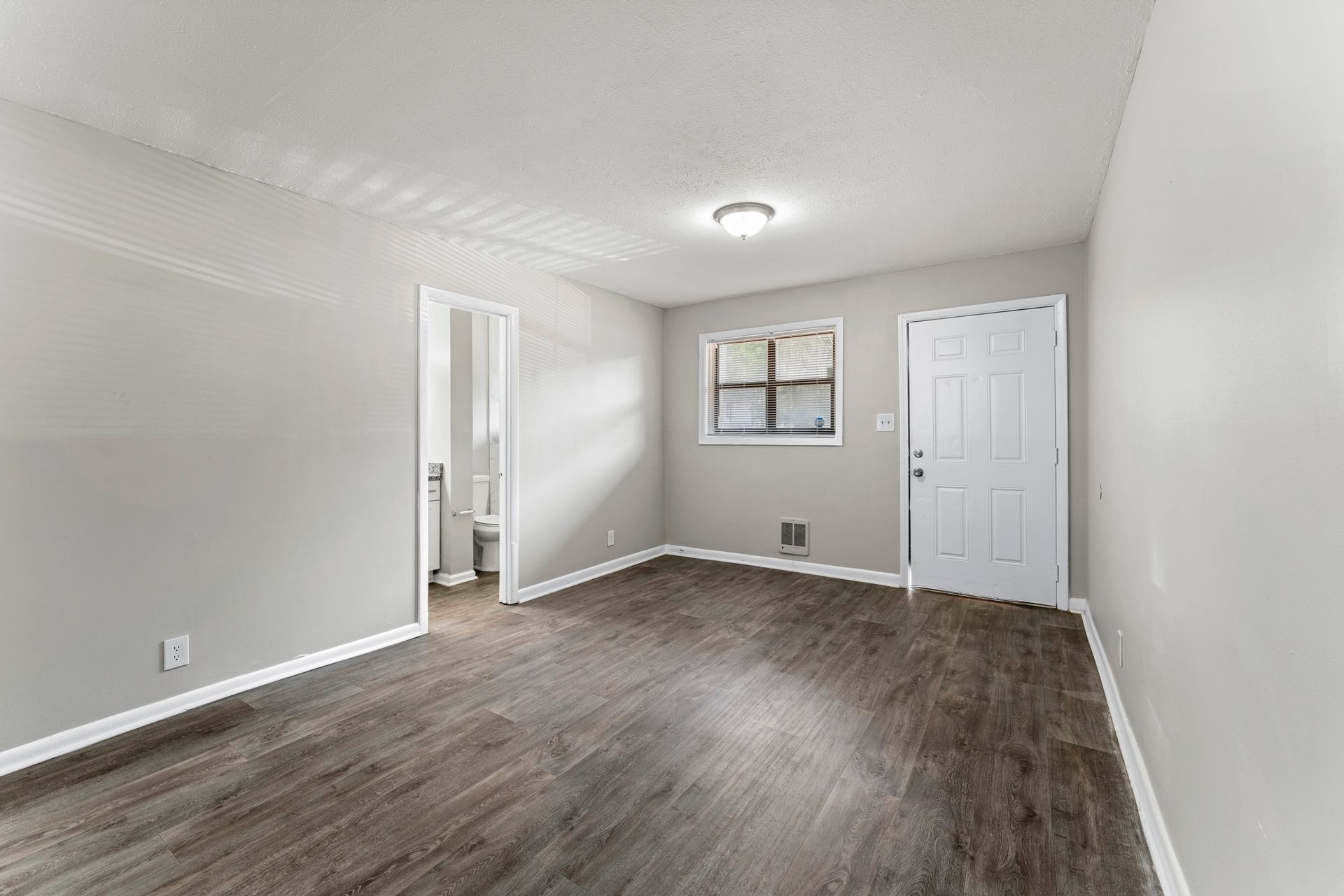 Empty modern bedroom with gray walls, wood-look floor, white doors, and a small window with blinds