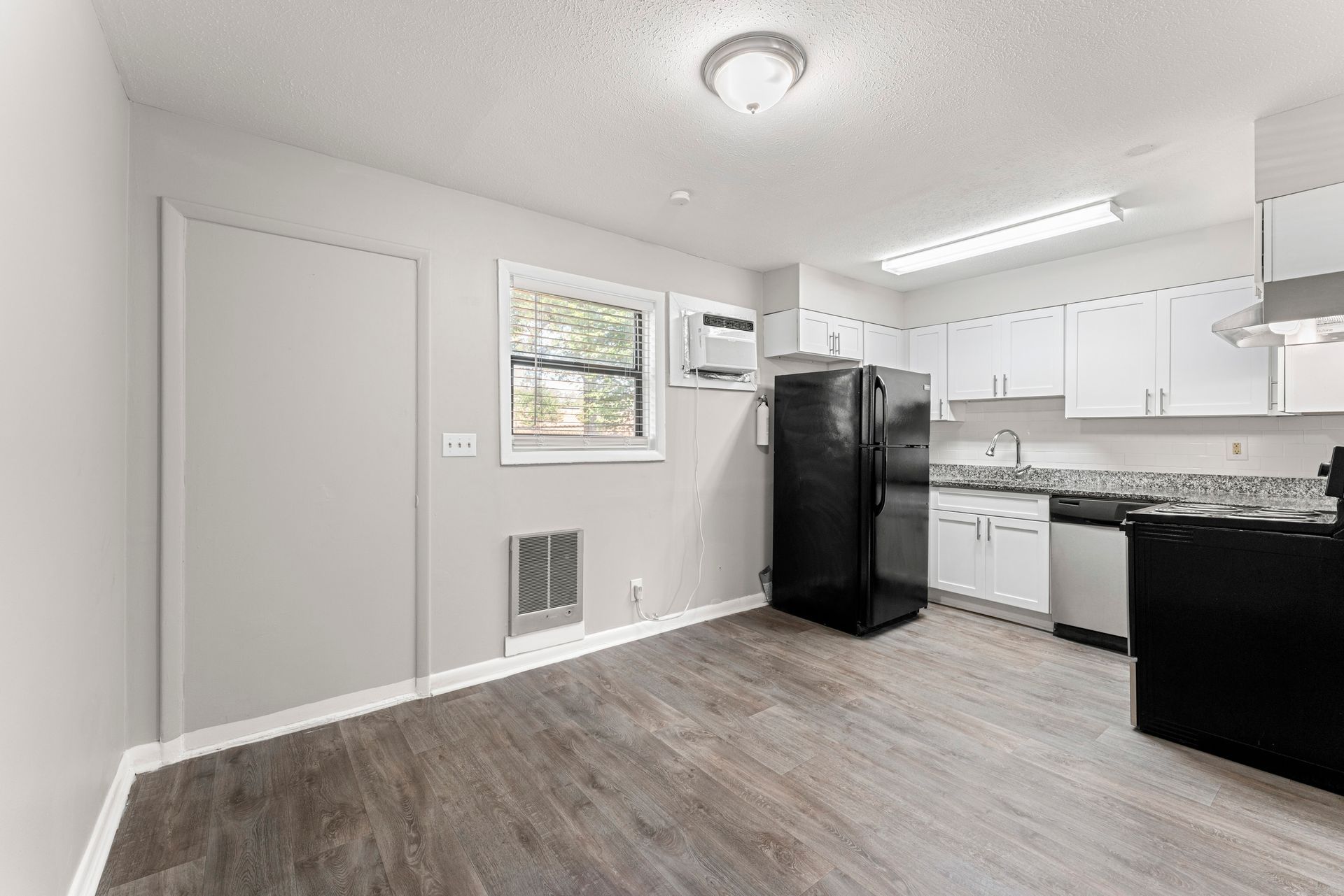 Bright kitchen with white cabinets, black refrigerator and stove, and gray wood-look flooring