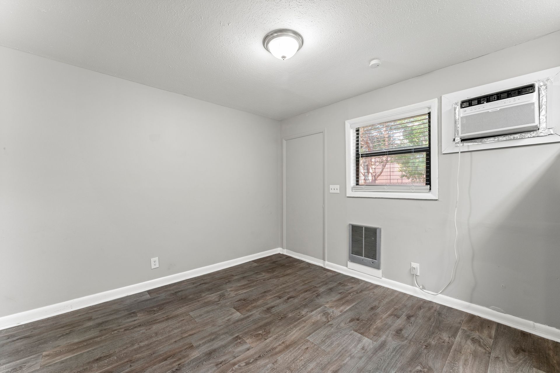 Empty gray room with wood flooring, window AC unit, window, and wall vent