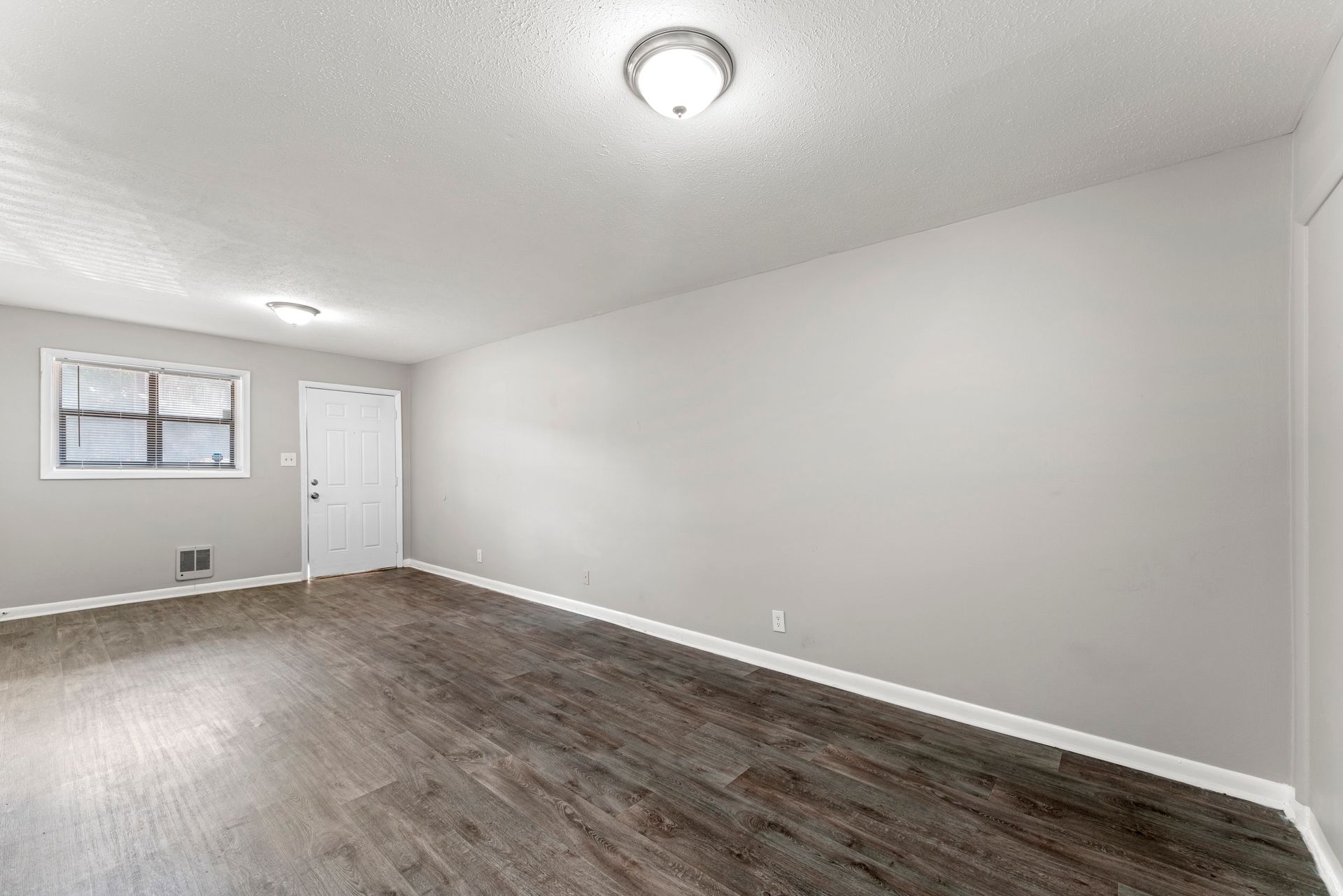 Empty gray room with wood-look floor, white ceiling, window, and door
