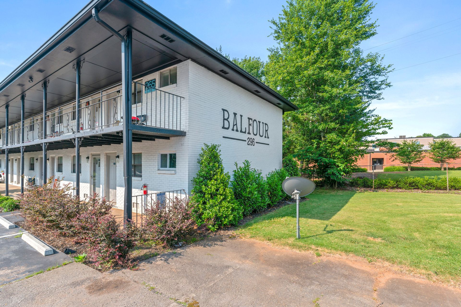 Exterior of a two-story motel with balconies, sign reading “BAL HOTEL,” and a grassy yard under clear skies
