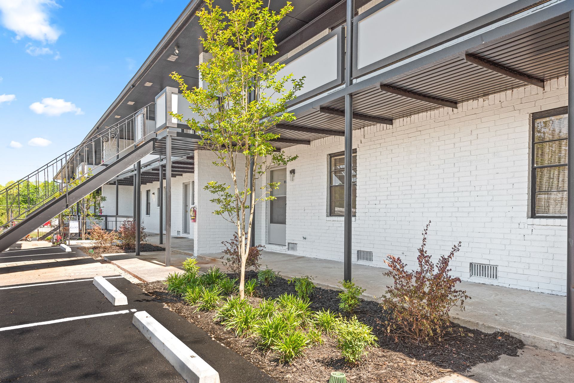 Modern apartment building exterior with balconies, white brick walls, and landscaped walkway