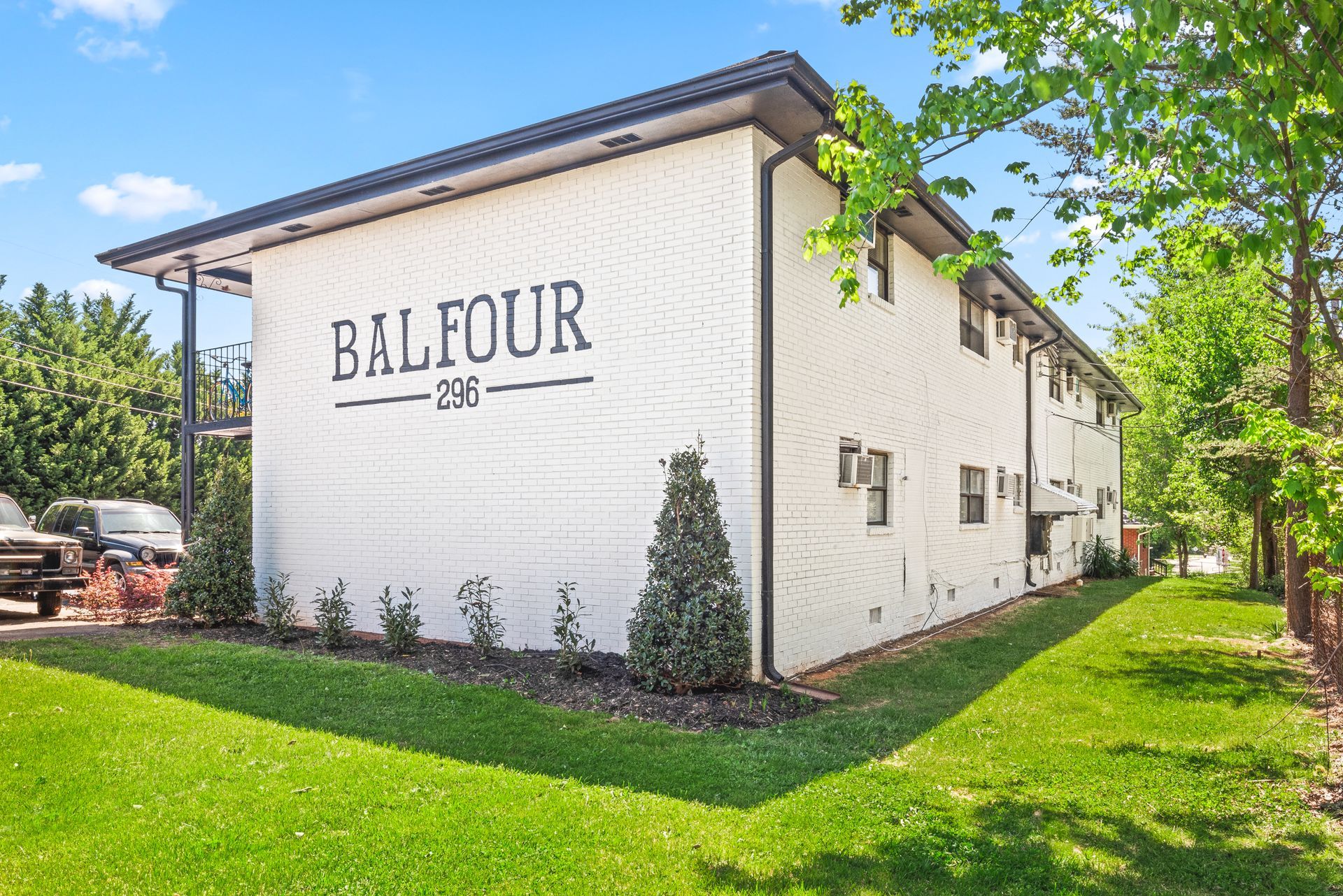 White Balfour building with white brick walls, green lawn, and trees on a sunny day