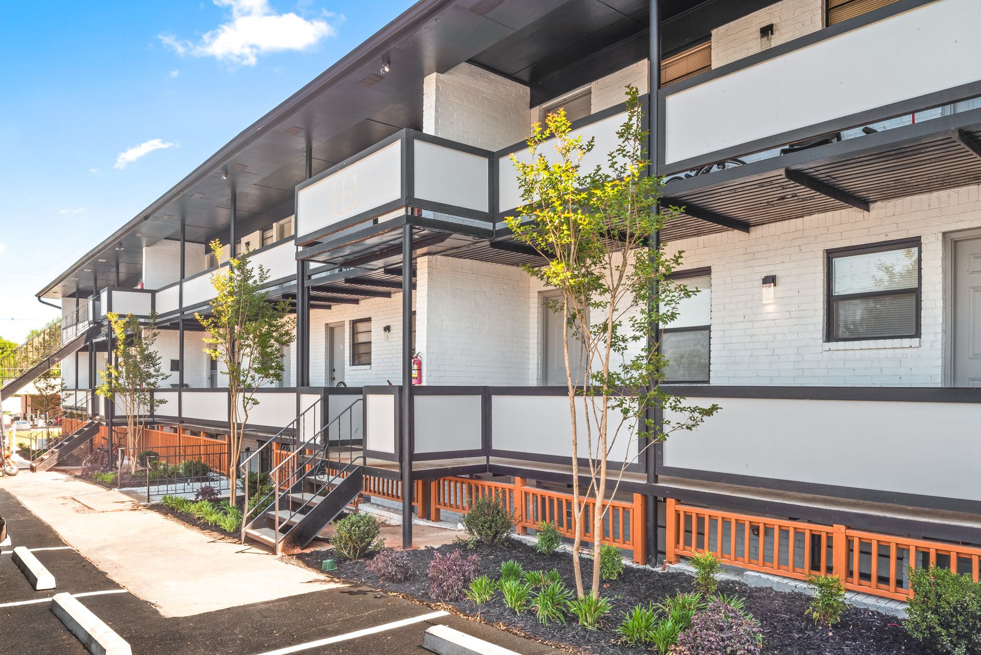 Modern apartment building with balconies, white walls, dark trim, and landscaped walkway in sunlight
