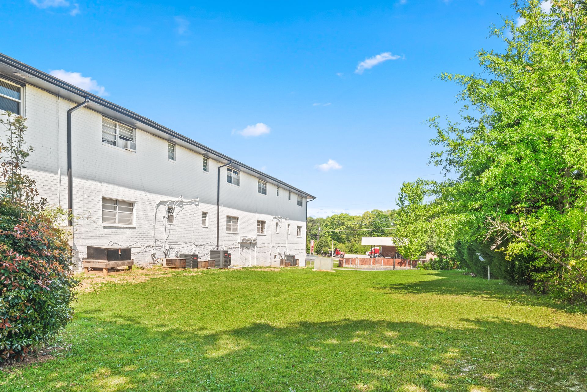 White two-story building beside a grassy yard and trees under a bright blue sky