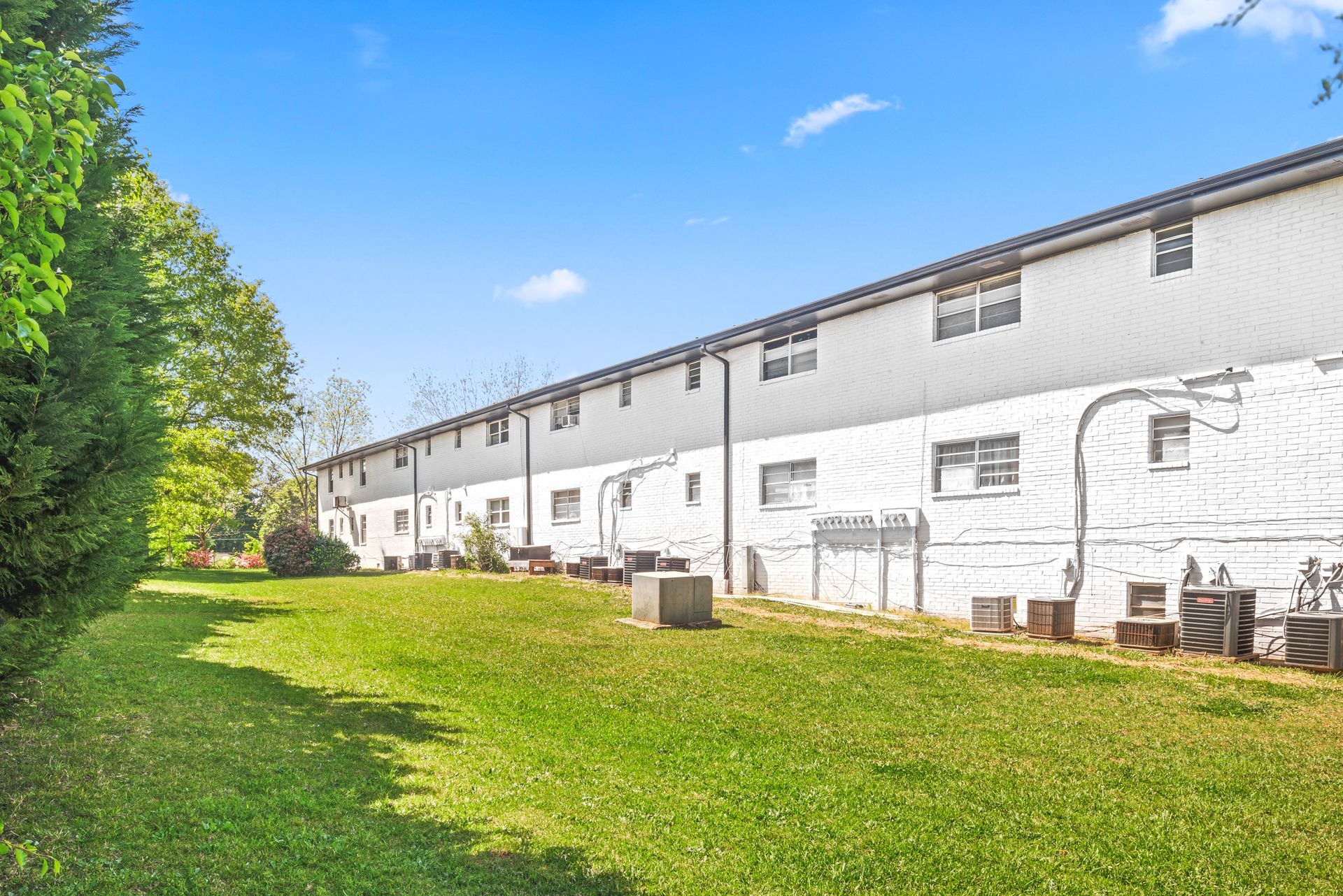 Row of white apartment buildings beside a green lawn under a bright blue sky