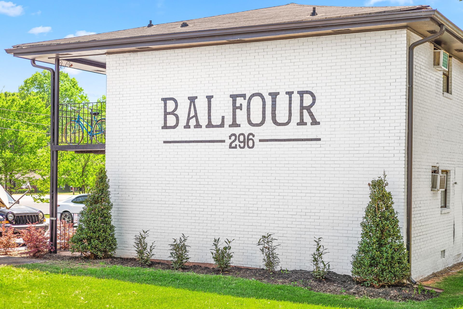 White brick building with “BALFOUR 298” sign, trimmed shrubs, and green lawn.