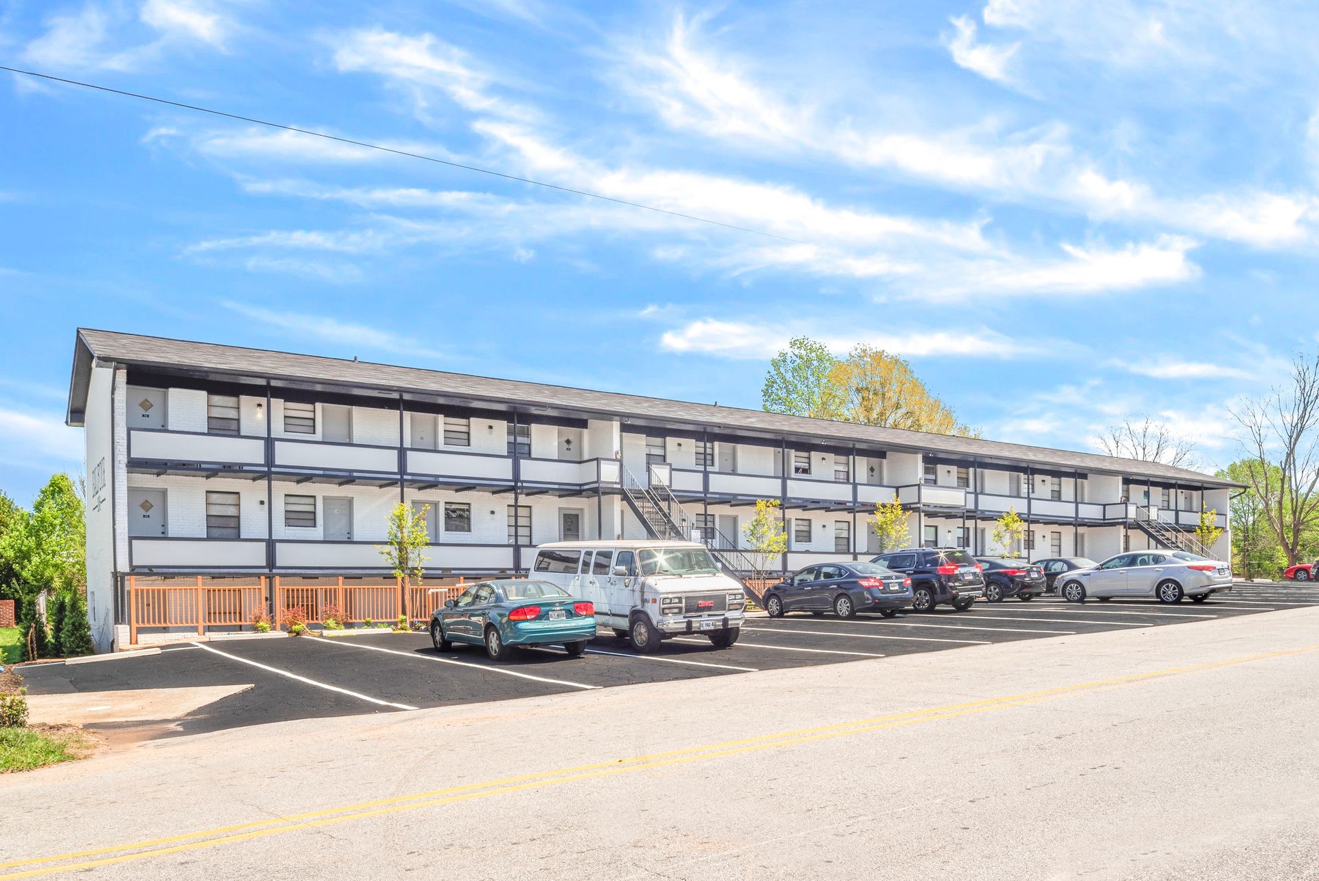 Long apartment building with parked cars under a bright blue sky