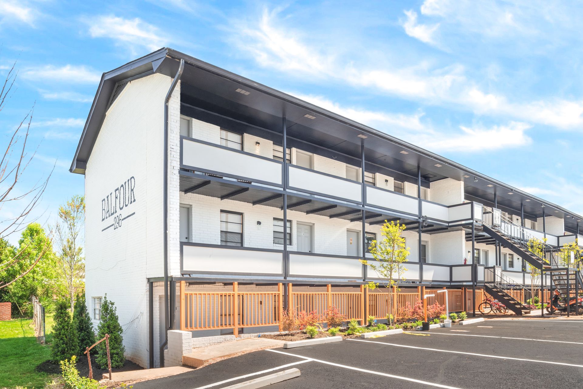 Modern three-story apartment building with balconies, white and gray exterior, and parking lot under blue sky