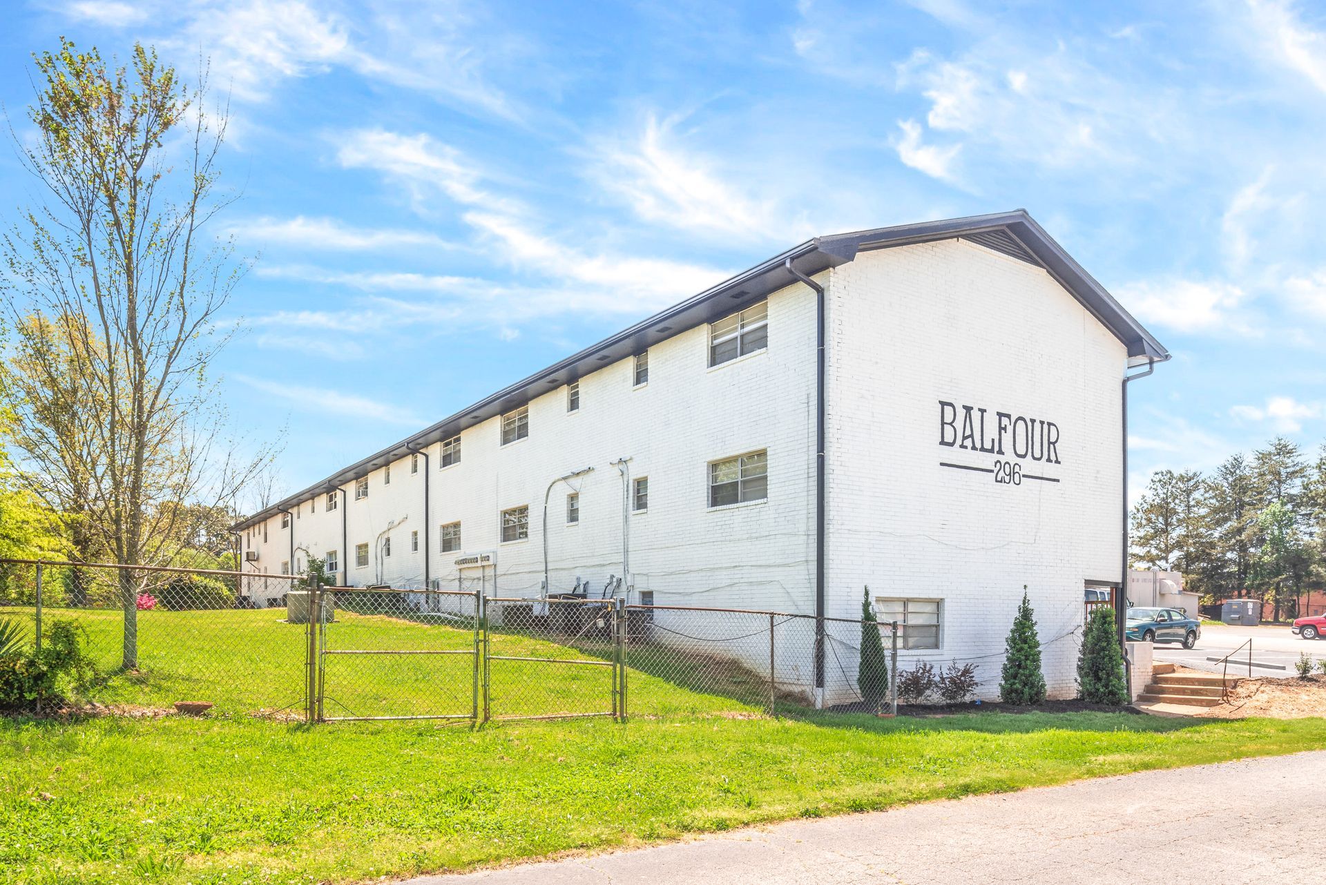 White two-story building with “BILTON” sign beside a fenced grassy area under a blue sky