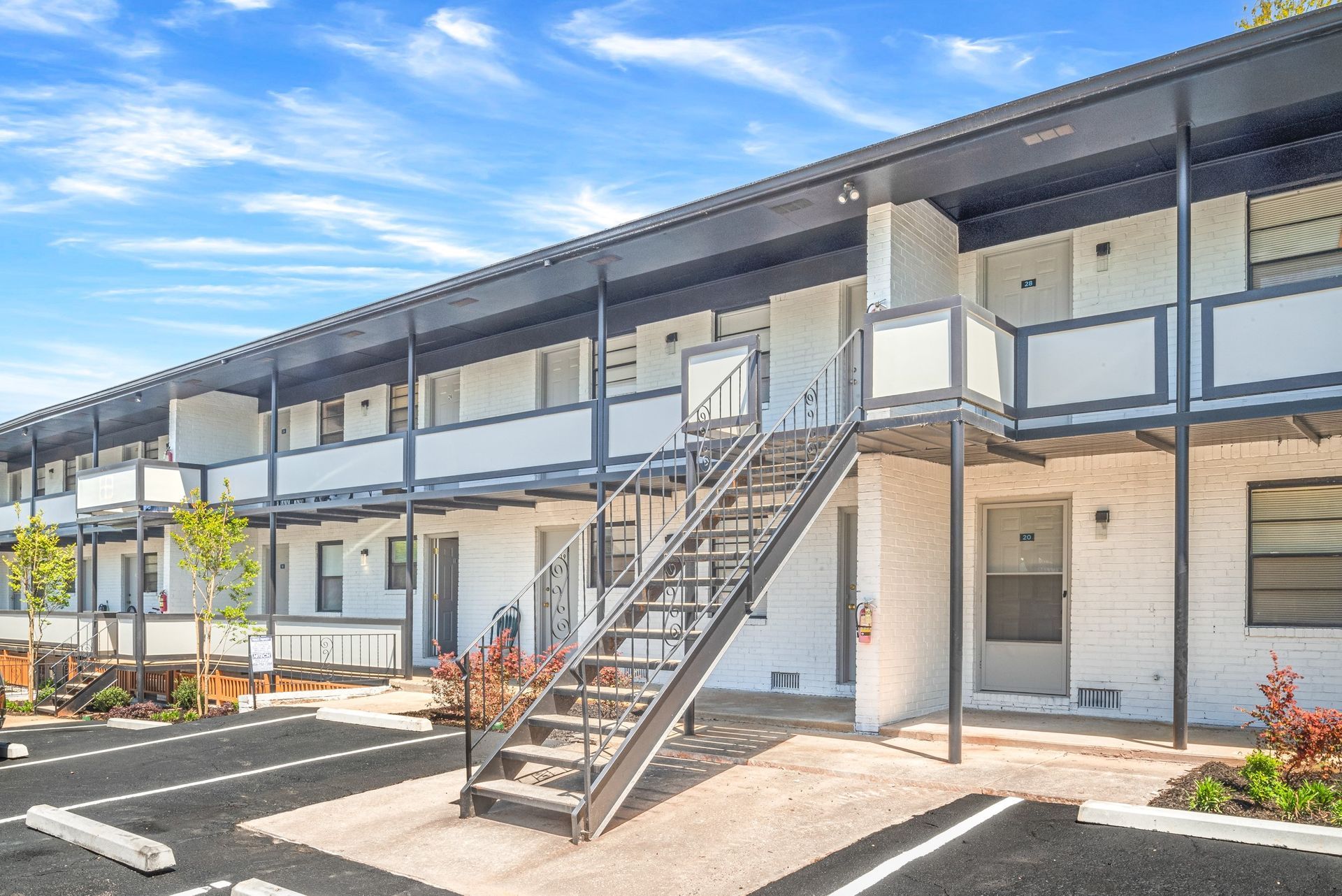 Two-story apartment building with exterior staircases and balconies on a sunny day